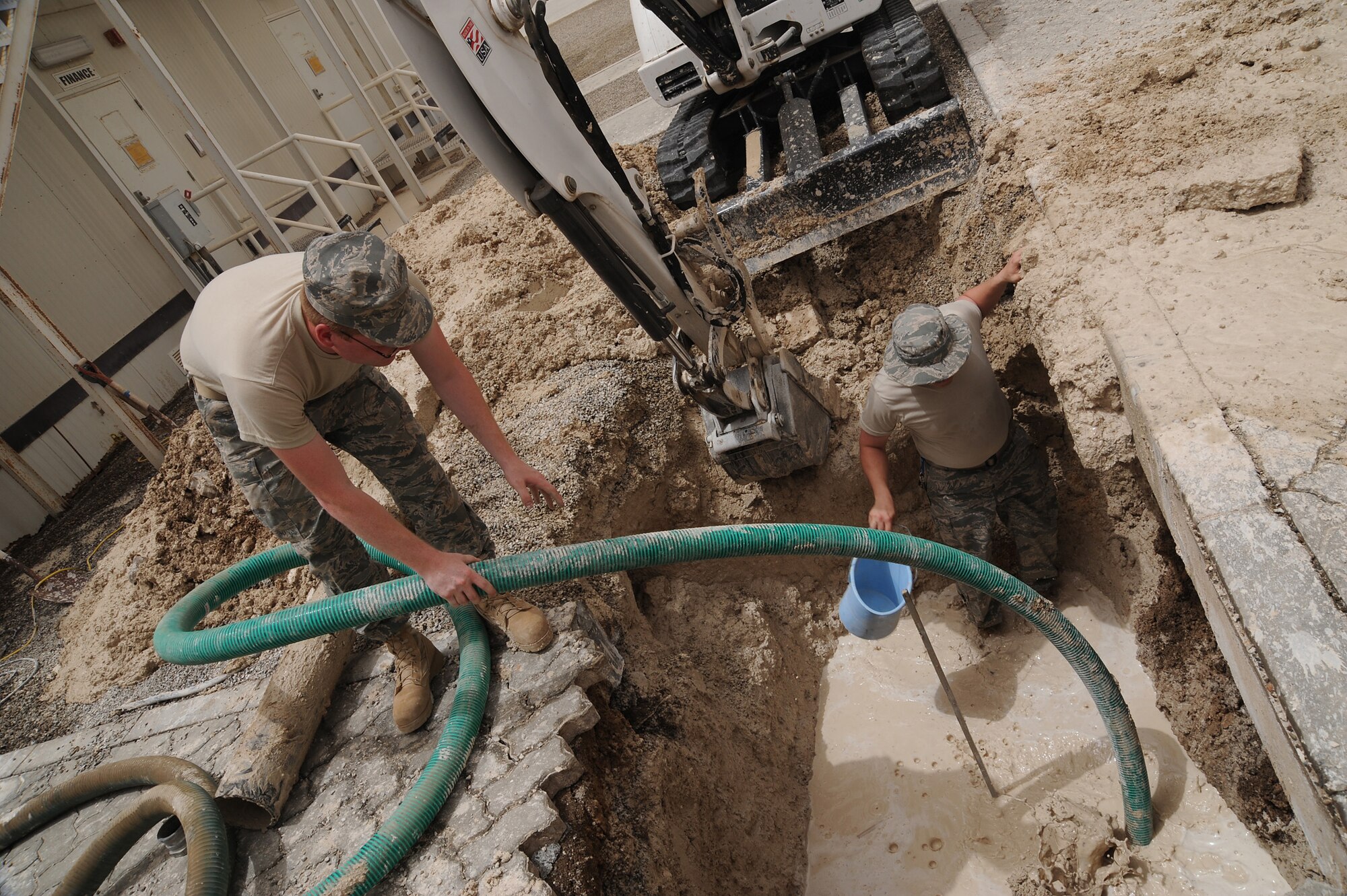 SOUTHWEST ASIA - Senior Airman Adam Stoll and Airman 1st Class Justin Vaughn, 380th Expeditionary Civil Engineer Squadron utility craftsmen, use a water pump and a bucket to drain water from a hole dug to find a leaking water pipe, July 6 in Southwest Asia. The pipe sprung a leak when the mechanical flange that connects the valve to the pipe lost its seal. (U.S. Air Force photo by Senior Airman Brian J. Ellis) 