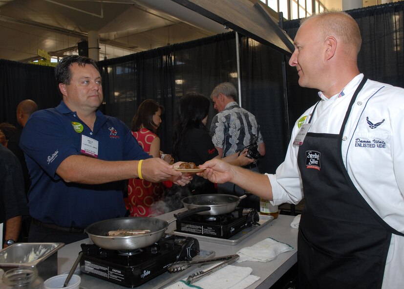 Tech. Sgt. Damon Vitale, Pacific Air Forces commander's enlisted aide, serve event exhibitor Kelly Wall an order of oven smoked lamb riblets iat the 15th Annual Hawaii Lodging, Hospitality and Foodservice Expo at the Neal Blaisdell Center in Honolulu, Hawaii, July 9. Sergeant Vitale, along with Master Sgt. Craig Duclos, senior enlisted aide, prepared and served numerous dishes including shrimp, steak and swordfish, during their first participation in the expo. (U.S. Air Force photo/Tech. Sgt. Jerome S. Tayborn)
