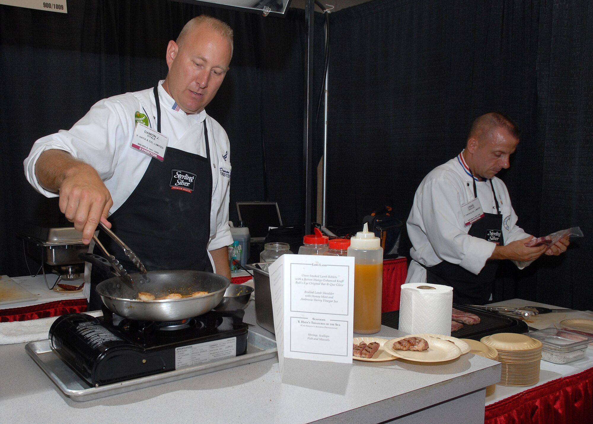 Tech. Sgt. Damon Vitale, Pacific Air Forces commander's enlisted aide, and Master Sgt. Craig Duclos, senior enlisted aide, prepare shrimp and steak at the 15th annual Hawaii Lodging, Hospitality and Foodservice Expo at the Neal Blaisdell Center in Honolulu, Hawaii, July 9. The two enlisted aides prepared and served numerous meat dishes during their first particpation in the expo..   (U.S. Air Force photo/Tech. Sgt. Jerome S. Tayborn) 