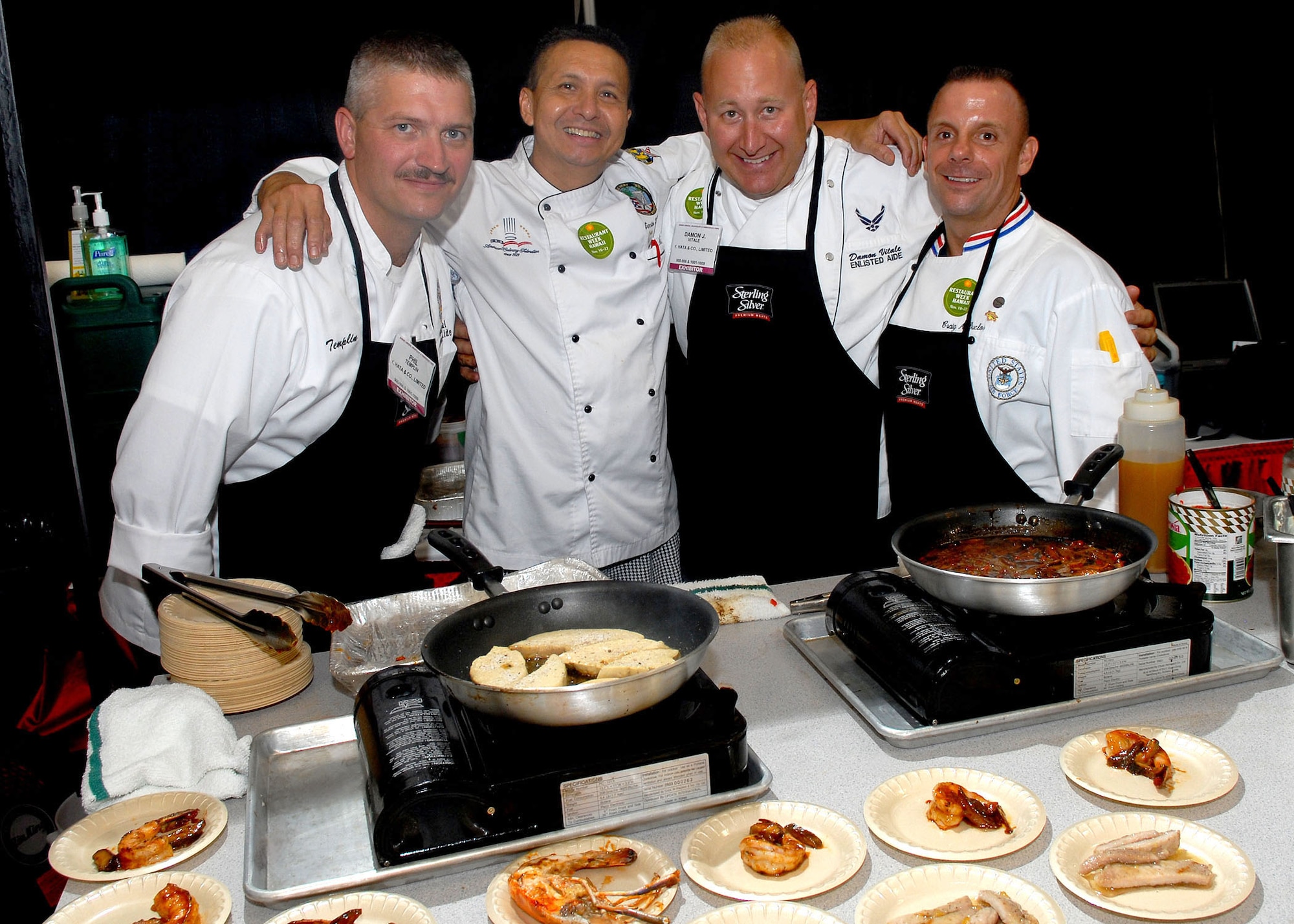 HONOLULU, Hawaii -- (From left to right) U.S. Coast Guard Chief Petty Officer Phil Templin, command aide, Ernesto Limcaco, corporate executive chef at Y. Hata & Company, Tech. Sgt. Damon Vitale, Pacific Air Forces commander’s enlisted aide, and Master Sgt. Craig Duclos, PACAF commander’s senior enlisted aide, get together at the VIP booth at the 15th Annual Hawaii Lodging, Hospitality and Foodservice Exposition at the Neal Blaisdell Center in Honolulu, Hawaii July 9.   The two enlisted aides, from Hickam Air Force Base, Hawaii, participated in the expo by cooking and serving meat entrees such as shrimp, steak and swordfish.  (U.S. Air Force photo/Tech. Sgt. Jerome S. Tayborn)  