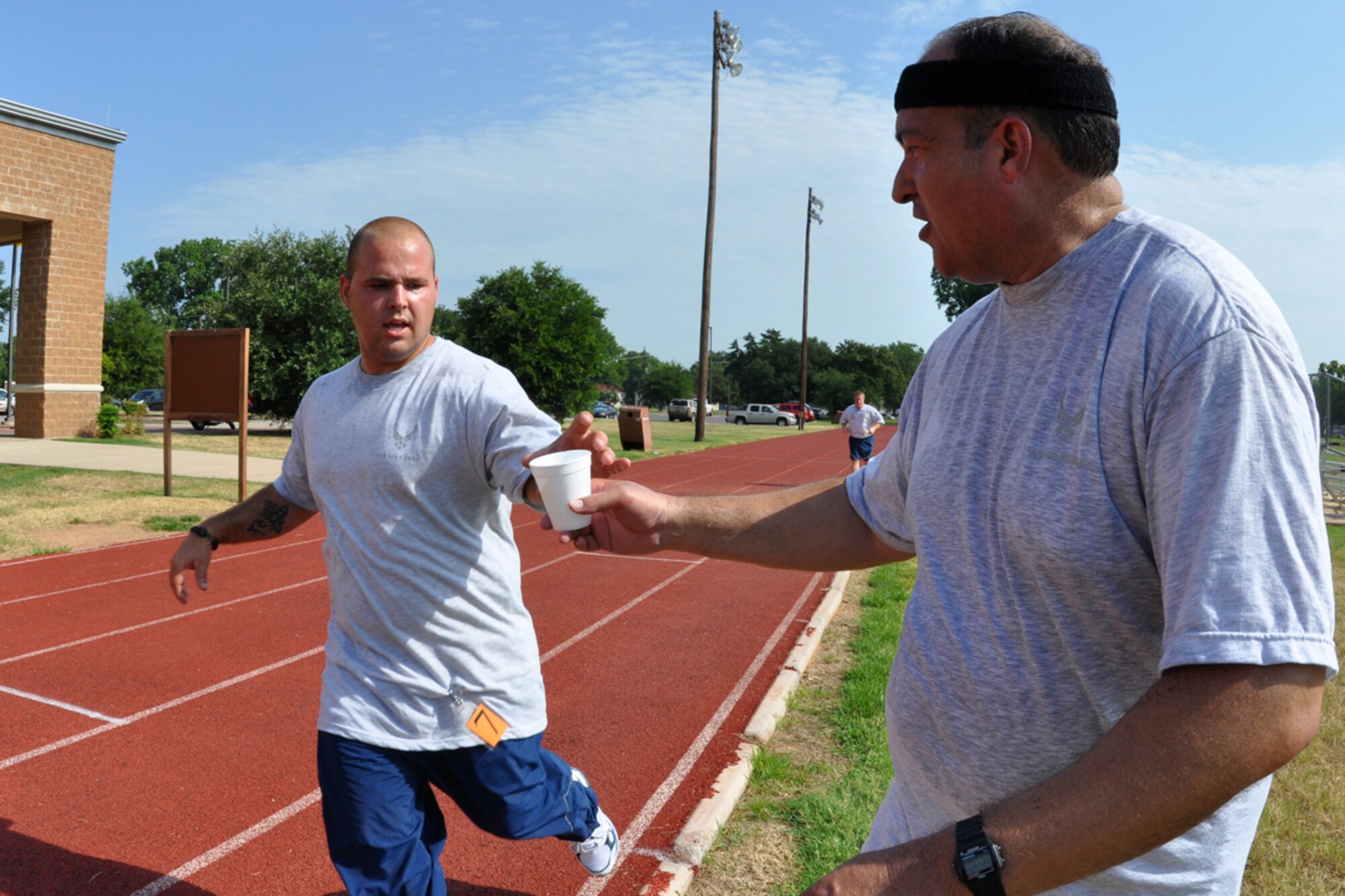 Senior Airman James Beusch, 917th Civil Engineer Squadron, HVAC mechanic, receives a cup of water from Lt. Col. Charles Morgan, 917th Wing, process manager, during his fitness test on the outdoor track at Barksdale Air Force Base, La., July 12, 2009. After completing his own fitness test, Colonel Morgan passed out water to other runners who were still involved in the annual event. The Air Force Fitness Test is designed to test the body composition, muscular strength/endurance and cardiovascular respiratory fitness of Airmen in the U.S. Air Force. As part of the “Fit to Fight” program, the Air Force adopted a more stringent physical fitness assessment; the new fitness program was established on January 1, 2004, and replaces the annual ergo-cycle test that Air Force used before. (U.S. Air Force photo/Tech. Sgt. Jeff Walston)