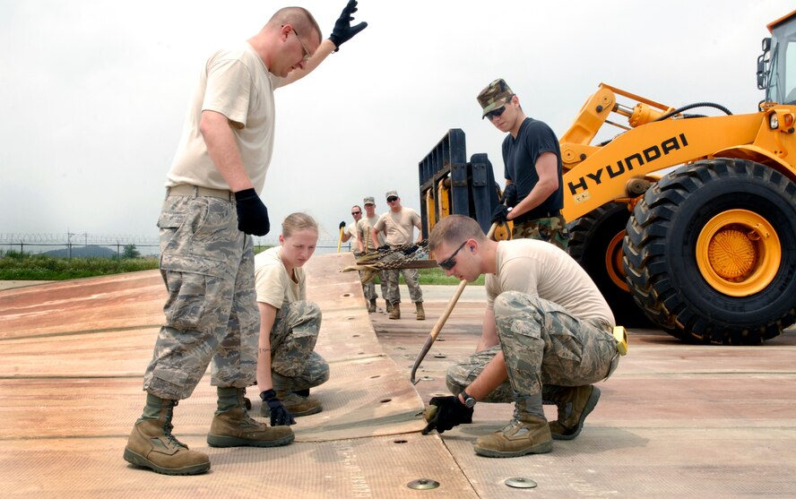 Airmen from the 51st Civil Engineering Squadron guide a folded fiberglass mat into place during airfield damage repair training at Osan Air Base, Republic of Korea, July 15.  The 30x54 foot mats are used to quickly repair runway damage, and can be connected to cover a large areas. (U.S. Air Force photo/Senior Airman Stephenie Wade)