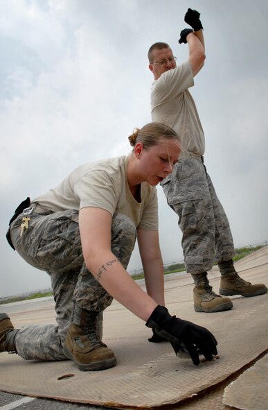 Senior Airman Candice Otis, with the help of a spotter, connects two folded fiberglass mats together during airfield damage repair training at Osan Air Base, Republic of Korea, July 15.  The 30x54 foot mats are used to quickly repair runway damage, and can be connected to cover a large areas. Airman Otis is part of the 51st Civil engineering Squadron. (U.S. Air Force photo/Staff Sgt. Brian Ferguson)