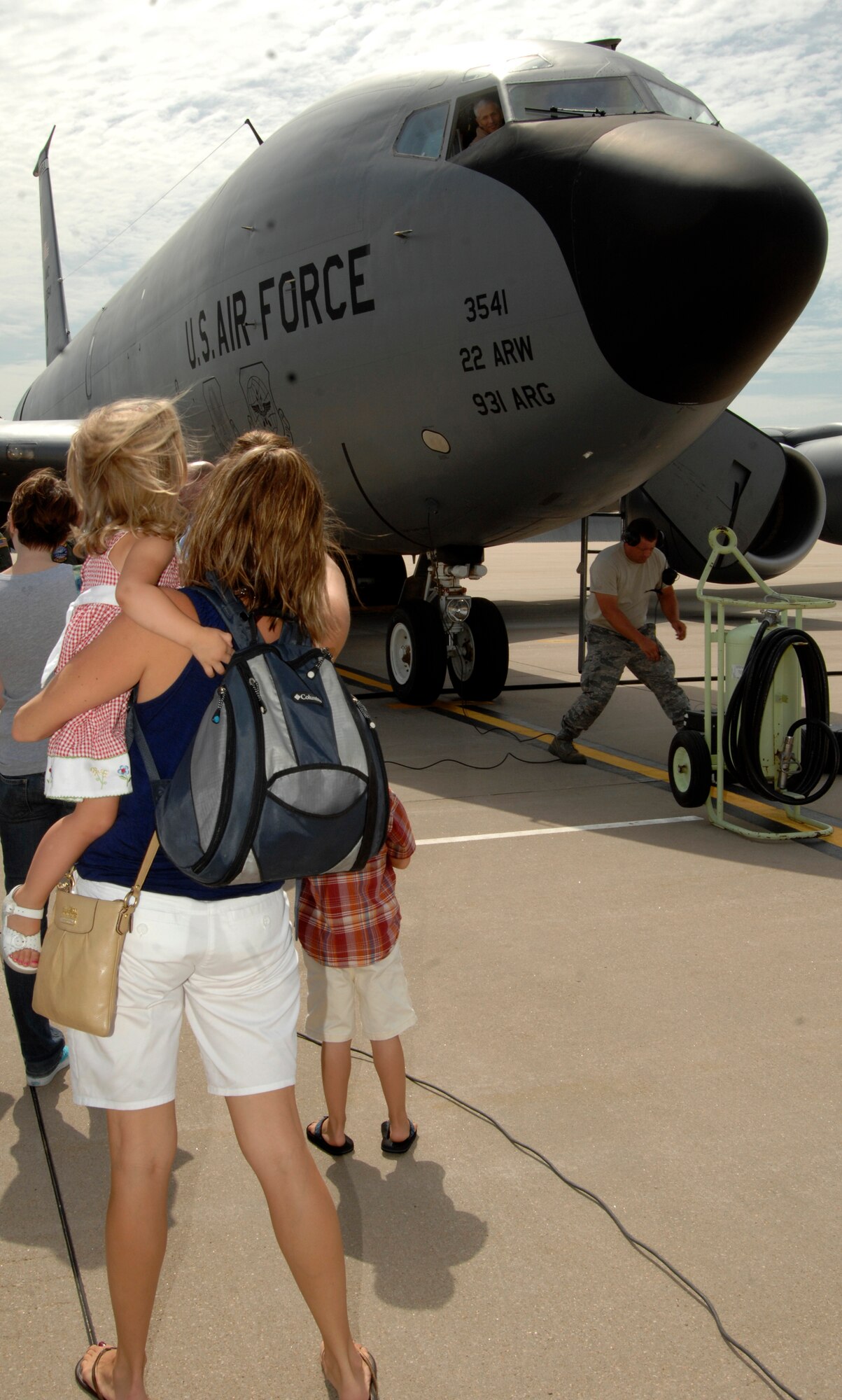 MCCONNELL AIR FORCE BASE, Kan. -- Trisha Hughes waves to her husband, Capt. Ryan Hughes, 344th Air Refueling Squadron, flying a KC-135 Stratotanker while holding their daughter Amelia, 2, and son Oliver, 4, on the flightline, July 13. Captain Hughes had just returned from a 60-day rotation deployment. (Photo by Senior Airman Laura Suttles)