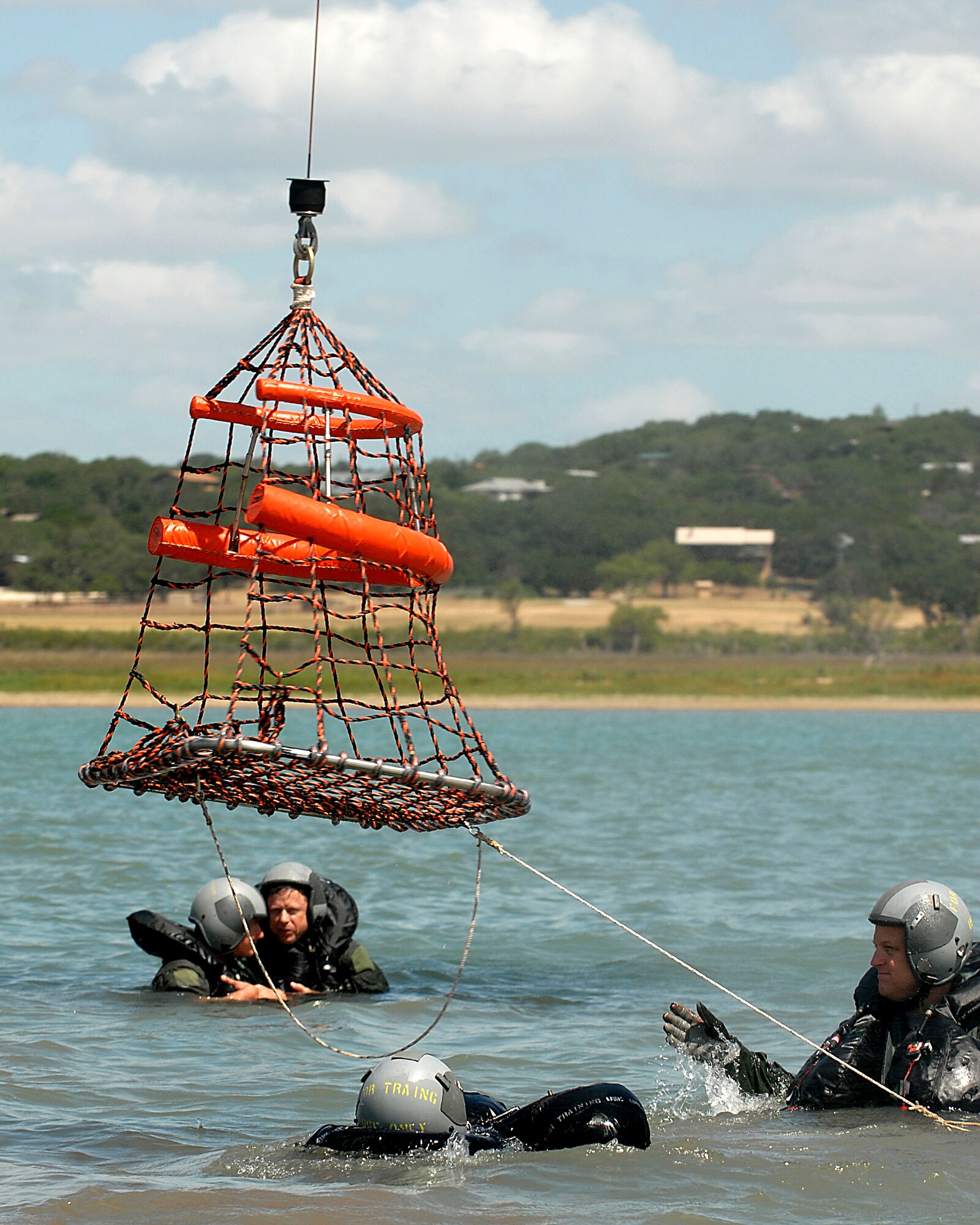 Lt. Col. Michael "Bones" McCoy (right), an F-16 pilot assigned to the 149th Fighter Wing, Texas Air National Guard, Lackland Air Force Base, Texas, guides an aerial rescue basket to other members.  Col. McCoy underwent water survival training as part of an annual training requirement at Canyon Lake, Texas, July 11, 2009.  (U.S. Air Force photo/Master Sgt. Robert Shelley)