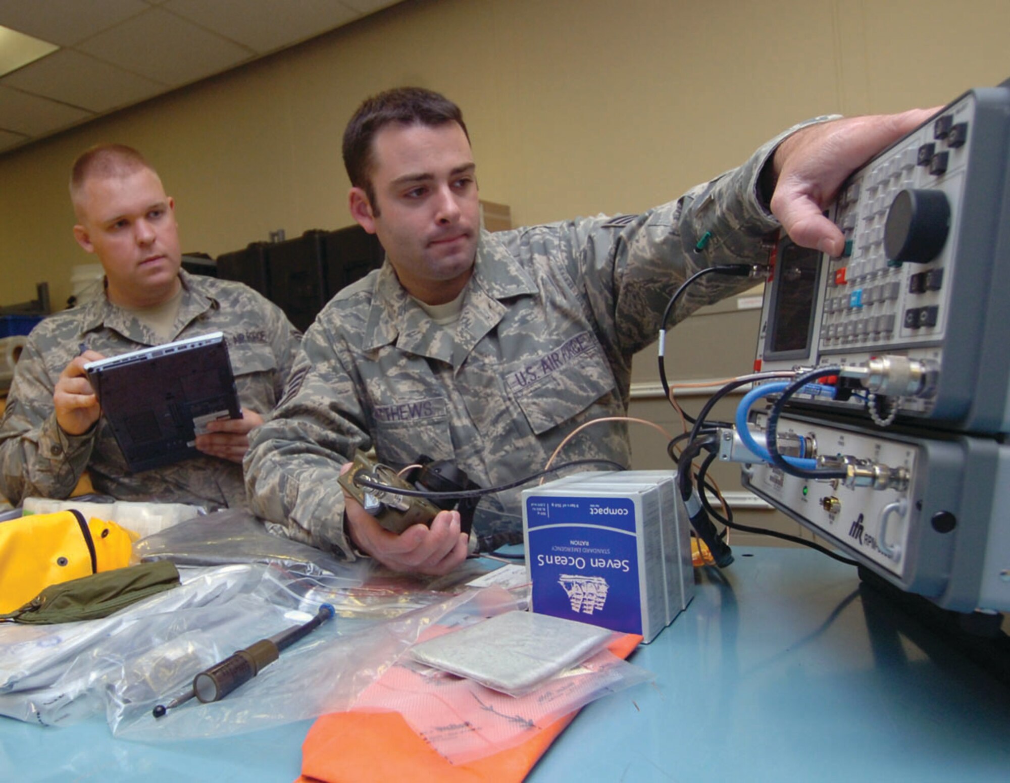 Senior Airman Stuart McCallum, left, 457th Airlift Squadron life support technician annotates in a digital technical order manual, as  Staff Sgt. Daniel Matthews, 457 AS aircrew flight equipment craftsman, performs a test on a PRC-90 radio used by pilots. The ten minute inspection includes several tests for the radio, such as frequency errors, battery signal strength and sound modulation. The radio which is part of the pilot’s T-9 life raft survival kit is tested bimonthly. (U.S. Air Force photo/ Bobby Jones)
