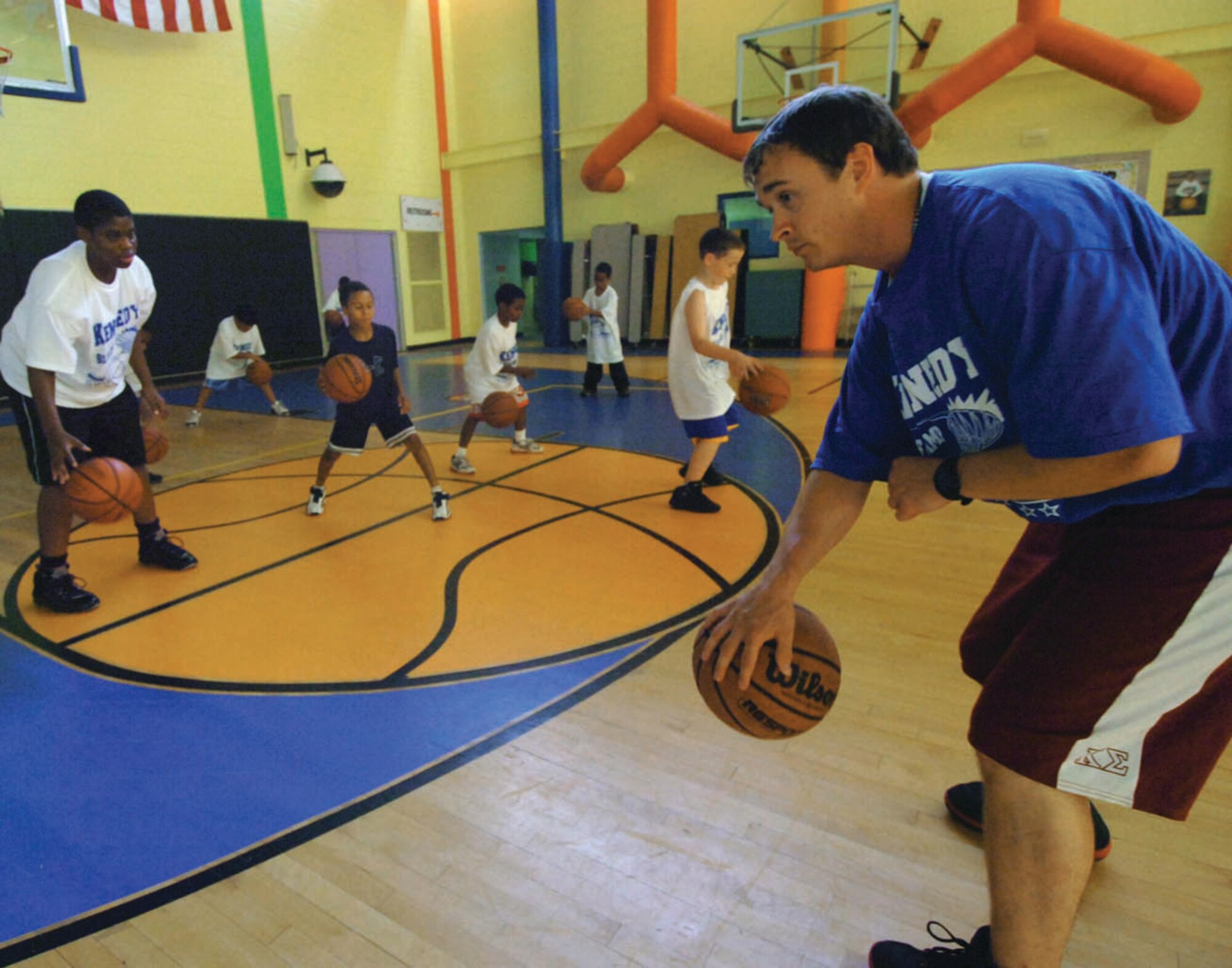 Mark McGaha gives a group of Andrews Youth Center children a hands-on drill in dribbling a basketball during the Third Annual Kennedy Skills Basketball Camp held at the Youth Center July 10. The week-long, training camp provided boys and girls basic basketball fundamentals and promoted the idea of team work, good attitudes, respect and sportsmanship. (U.S. Air Force photo/ Bobby Jones)