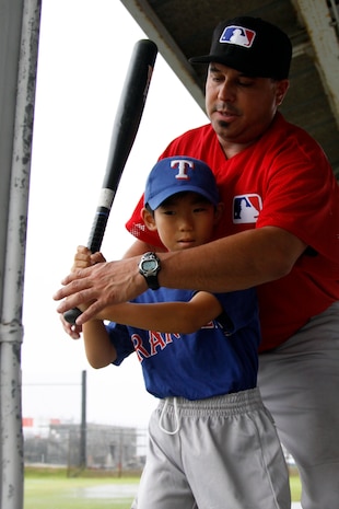 Major League Envoy Coach David Palese gives hands on training to a local Japanese child at the Penny Lake Pavilion here during a baseball clinic hosted by the Boys and Girls Club Youth and Teen Center here July 17. The clinic concentrated manly on swinging and batting techniques.