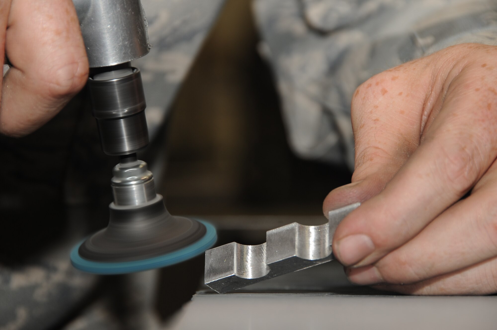Staff Sgt. Brandon Cotter, 28th Maintenance Squadron metals technician journeyman, uses a sanding disk to make sure a piece of hydraulic support block is completely smooth here, July 16.  The hydraulic support block will act as a hose clamp for hydraulic lines on the B-1 Lancer. (U.S. Air Force photo/Senior Airman Anthony Sanchelli)