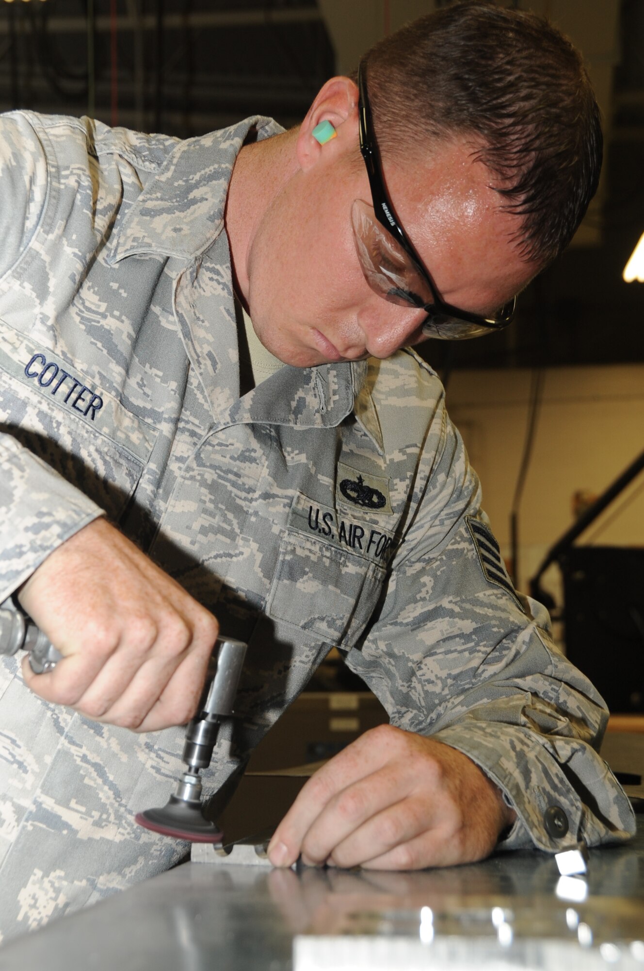 Staff Sgt. Brandon Cotter, 28th Maintenance Squadron metals technician journeyman, uses a sanding disk to make sure a piece of hydraulic support block is completely smooth here, July 16.  The hydraulic support block will act as a hose clamp for hydraulic lines on the B-1 Lancer. (U.S. Air Force photo/Senior Airman Anthony Sanchelli)