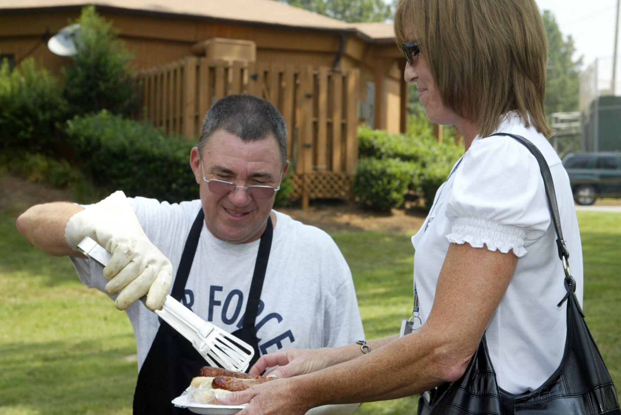 Tech. Sgt. Samuel Farmer, grill master, serves up a plate of sausages to Jeannie Goodwin of the 94th Communications Flight at the annual Corn and Sausage Roast held at Dobbins Lakeside July 15. The event featured grilled sausages, grilled corn and a mini car show. The annual fund raising event is held in support of Family Emergency Services, which provides aide to employees during emergencies. (U.S. Air Force photo/Don Peek)