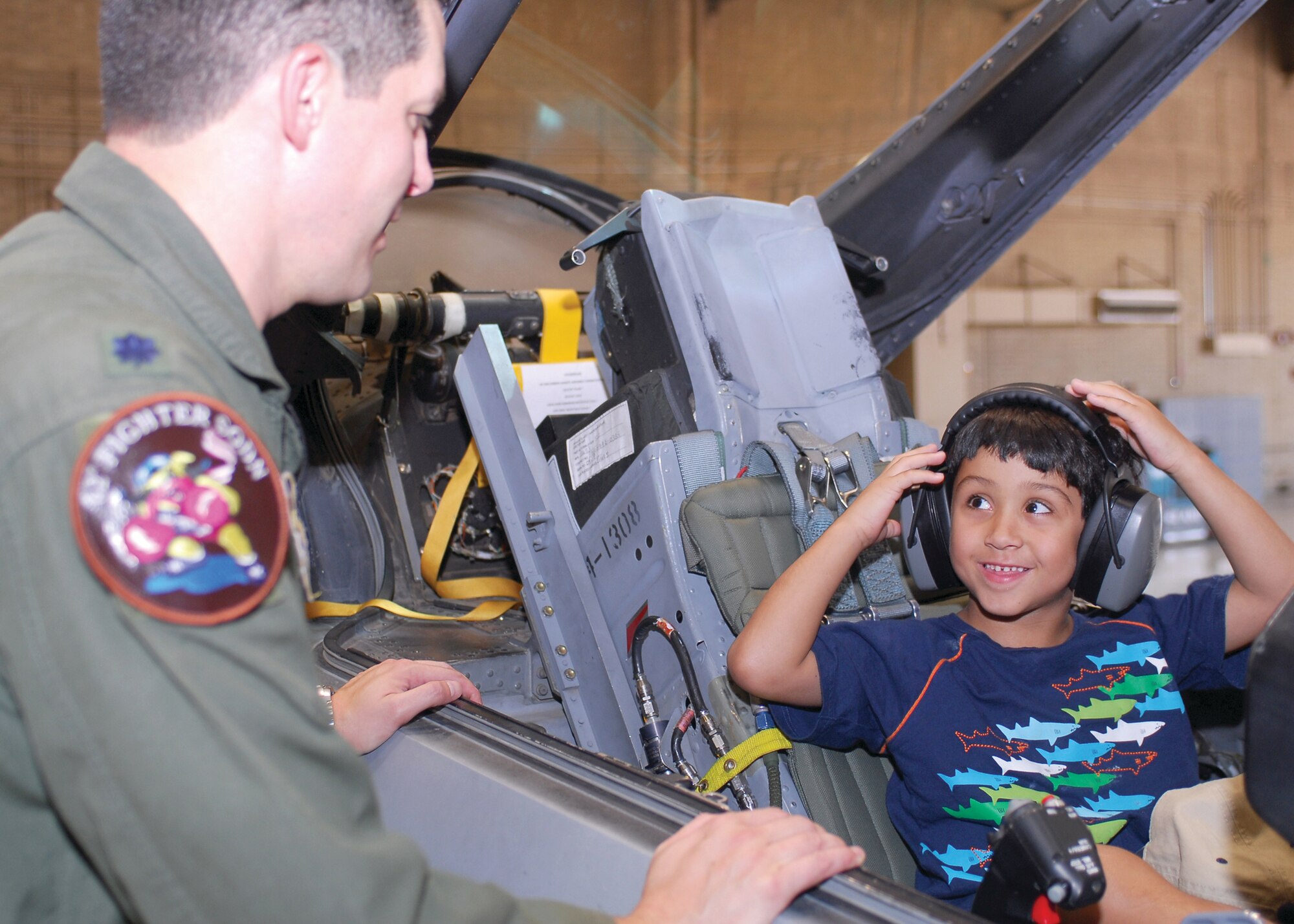 Pilot-of-the-day Kenneth "Junior" Serrano, 5, places a pair of headphones on while sitting in an F-16 Fighting Falcon parked in a hangar during his visit to Luke Air Force Base July 10. (U.S. Air Force photo by Senior Airman Tracie Forte)