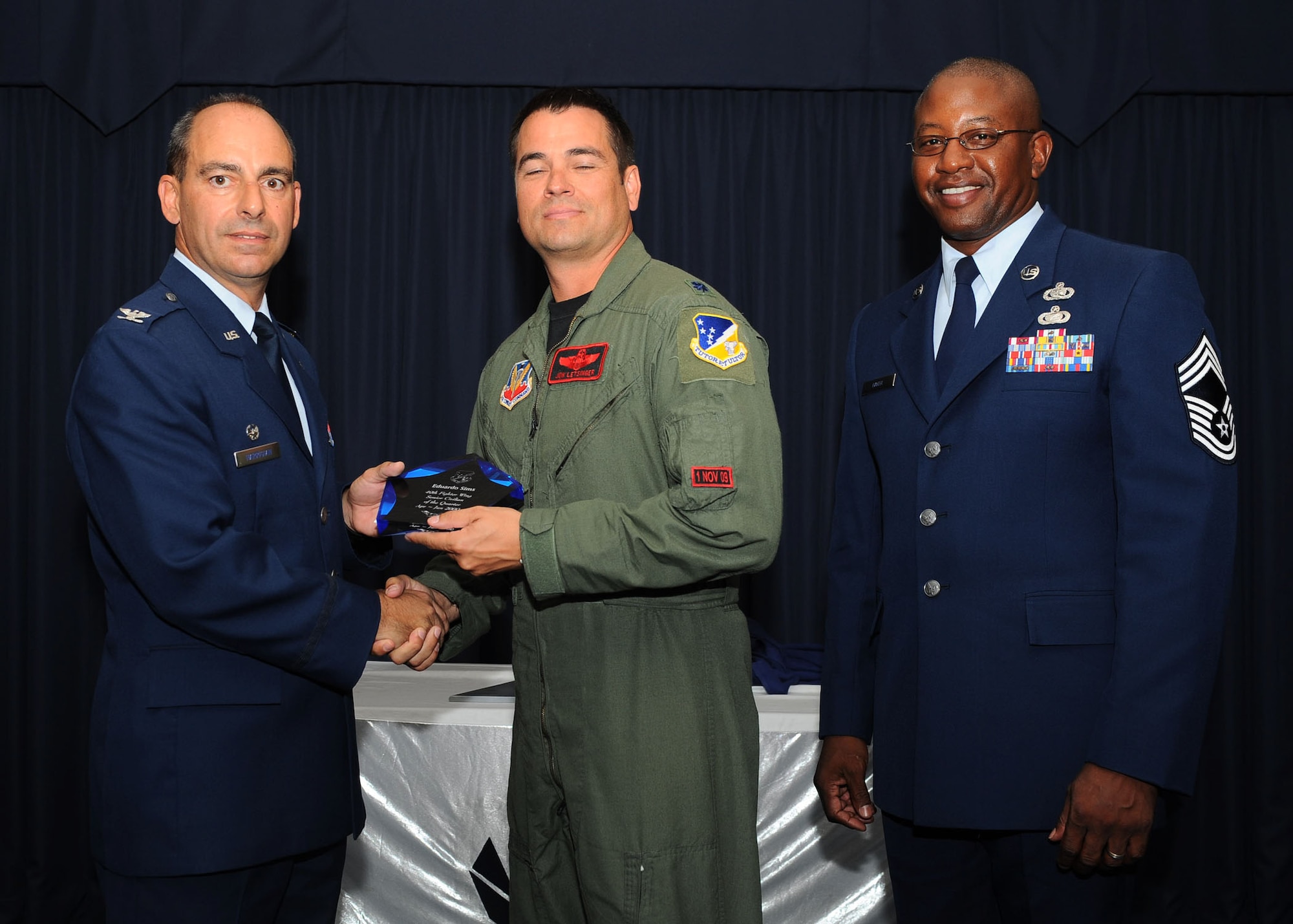 Col. Jeff Harrigian, 49th Fighter Wing commander, and Chief Master Sgt. Jerome Baker, 49th Mission Support Group, present the award for Wing senior civilian of the quarter to Lt. Col. John Letsinger, 49th Operations Support Squadron commander, who accepted the award on behalf of Mr. Eduardo Sims, 49 OSS, at Holloman Air Force Base, N.M., July 16.  The 49th Fighter Wing Quarterly Awards recognized the hard work of the 2nd quarter winners. 