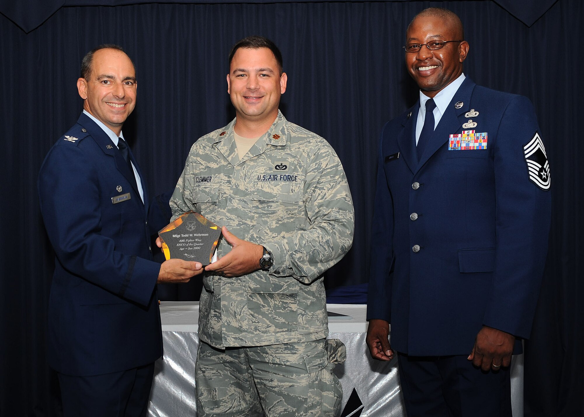 Col. Jeff Harrigian, 49th Fighter Wing commander, and Chief Master Sgt. Jerome Baker, 49th Mission Support Group, present the award for Wing senior non-commissioned officer of the quarter to Maj. Nathan Clemmer, Operations Flight commander who accepted the award on behalf of Master Sgt. Todd Wehrman, 49th Civil Engineers Squadron, at Holloman Air Force Base, N.M., July 16.  The 49th Fighter Wing Quarterly Awards recognized the hard work of the 2nd quarter winners. 