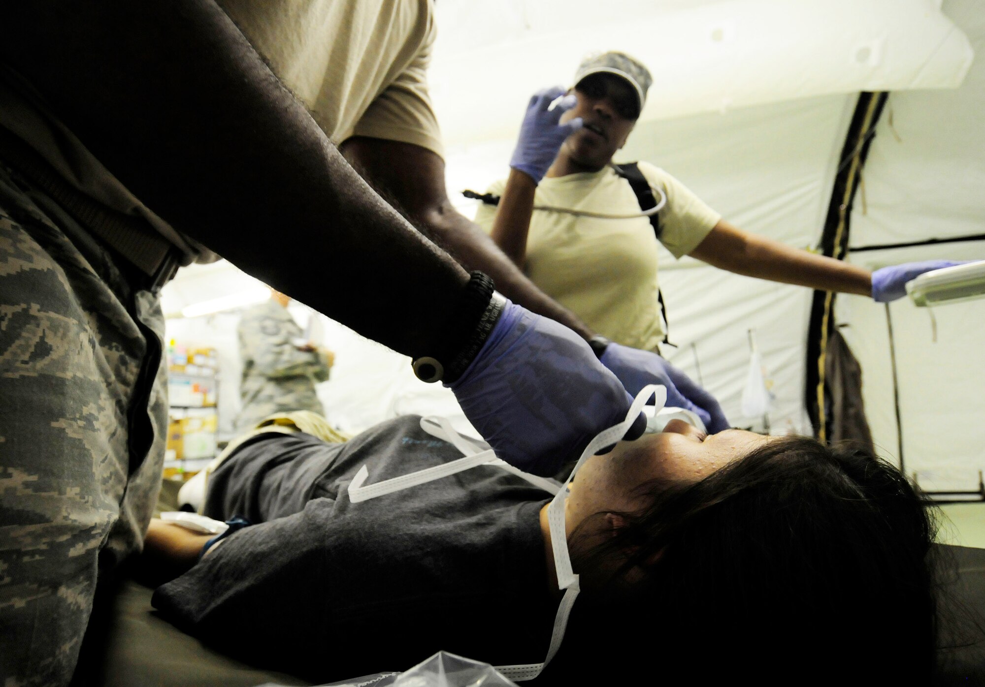 Staff Sgt. Brandy Verette explains to patient Airman 1st Class Jeanie Snyder what the procedure will be for her condition while Staff Sgt. Courtney Thompson applies a medical face mask during a simulated mass casualty exercise for the Humanitarian Assistance Rapid Response Team July 15 at Andersen Air Force Base, Guam. (U.S. Air Force photo/Airman 1st Class Courtney Witt)