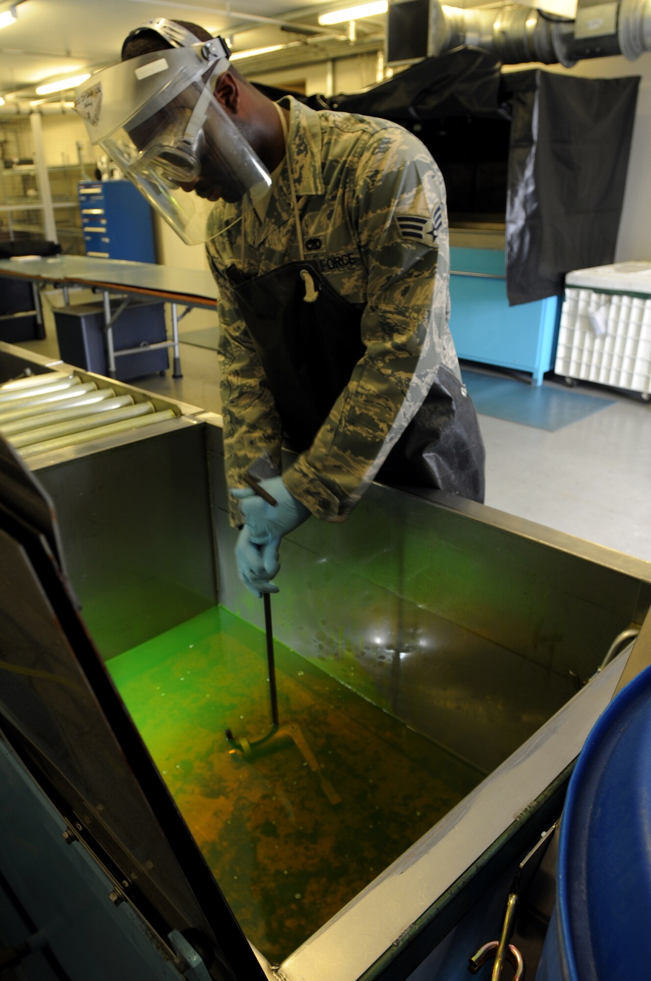 Senior Airman Joshua Robinson, 48th Equipment Maintenance Squadron Non-Destruction Inspection journeyman, dips a component into a chemical penetrent, which lights up under black light. After the component is dipped into the chemical, the surface is then cleaned, leaving only the fluorescence in the cracks of the component. This allows the cracks to be easily found when the fluorescence lights up under black light. (U.S. Air Force photo by Staff Sgt. Nathan Gallahan)