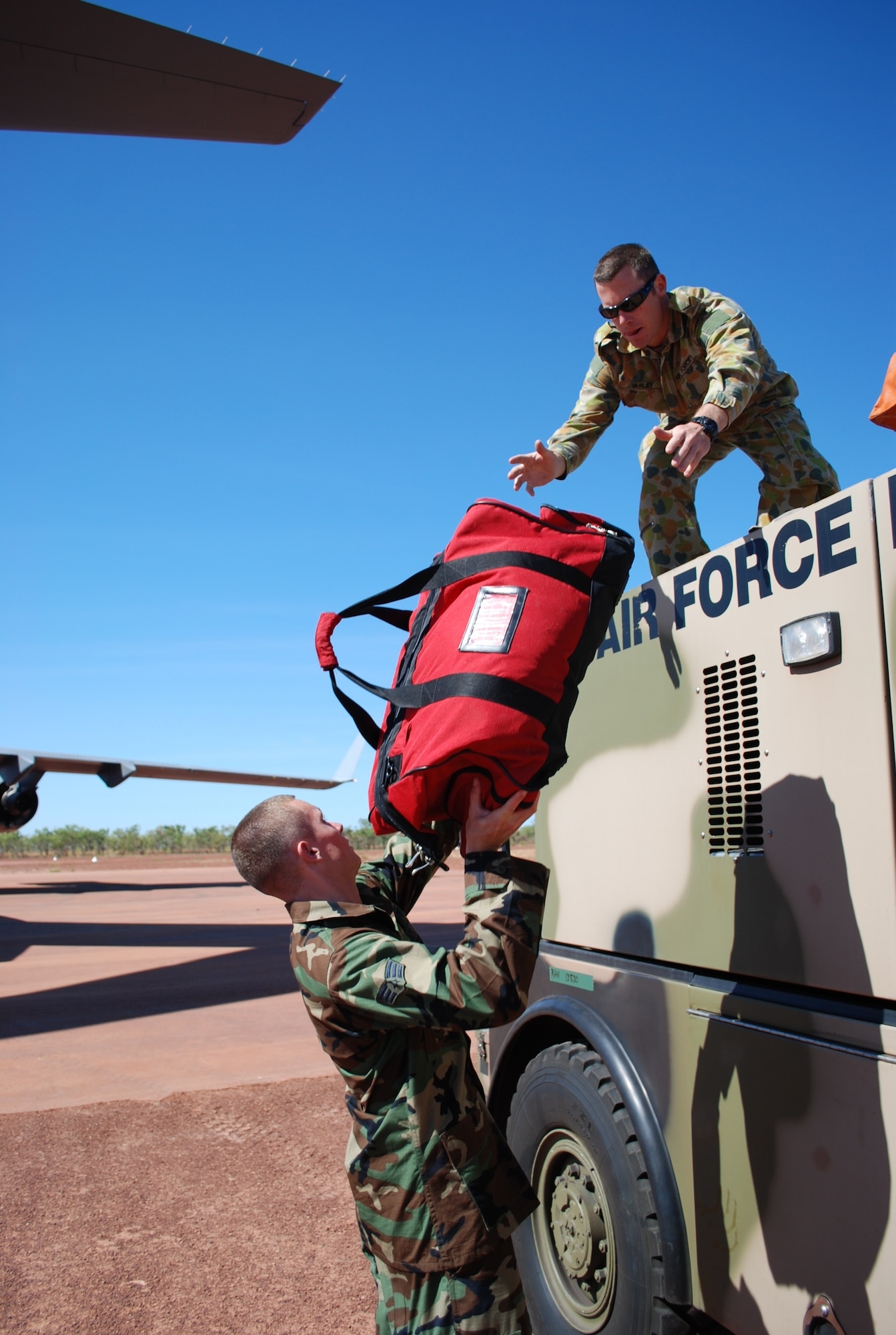 Senior Airman Shawn Pate, firefighter from the 3rd Civil Engineering Squadron, Elmendorf Air Force Base, Alaska, passes fire equipment to Leading Aircraftsman Liam Varley, an aviation rescue firefighter with the Royal Australian Air Force, at Bradshaw Field Training Area, Northern Territory, Australia, July 19. LAC Varley was loading the equipment on an E-One Titan fire engine as part of exercise Talisman Saber 2009. Airlifted for the first time ever on a C-17, the fire engine includes a Point of Entry Kit, which allows the fire team to remain in a remote area unsupported for up to 30 days. (Air Force photo/ Capt. Bryan Lewis) 
