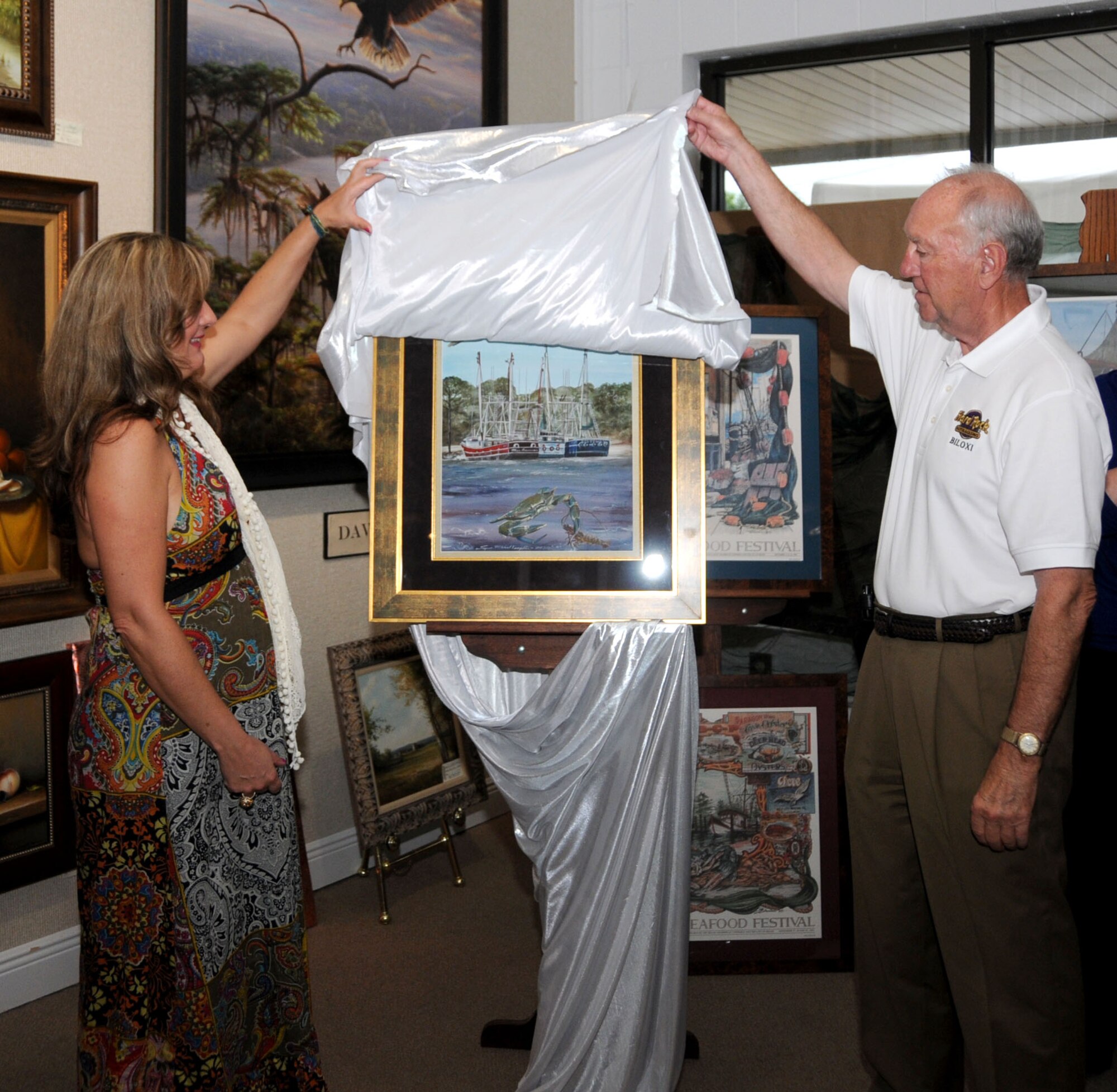 Keesler artist Suzy Templin, left, and Biloxi Mayor A.J. Holloway unveil Ms. Templin’s winning entry in the 28th annual Biloxi Seafood Festival poster contest, July 16.  Ms. Templin is a military fine artist employed by K-Mar Industries, the base’s multimedia contractor.  The three shrimp boats in the poster — the Miss Suzann, Three Musketeers and Big Temby — represent Ms. Templin, her three sons and her late husband, Tech. Sgt. John Templin, an instructor in the 338th Training Squadron, who was killed by a drunk driver 18 months ago.  Ms. Templin, who also won the contest in 1998, 1999, 2001 and 2003, won $500 for her winning entry.  This year’s festival is Sept. 12-13.  (U.S. Air Force photo by Kemberly Groue)