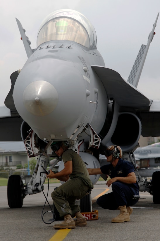Two Marine All-Weather Fighter Attack Squadron 533 maintenance Marines perform a maintenance check on an F/A-18 jet before takeoff at the VMFA(AW)-533 hangar here July 22. Approximately 140 of roughly 200 Marines who came with VMFA(AW)-533 are responsible for the safety and upkeep of about 10 F/A-18 squadron aircraft.