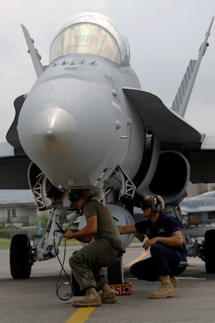 Two Marine All-Weather Fighter Attack Squadron 533 maintenance Marines perform a maintenance check on an F/A-18 jet before takeoff at the VMFA(AW)-533 hangar here July 22. Approximately 140 of roughly 200 Marines who came with VMFA(AW)-533 are responsible for the safety and upkeep of about 10 F/A-18 squadron aircraft.