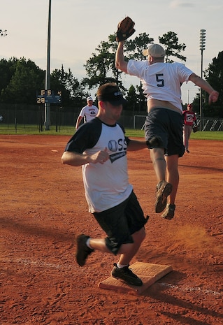 Michael Tate is safe at first base as Matthew Pease leaps to catch an overthrown ball during an intramural softball game here July 21. 437th Security Forces Squadron won against 437th Operations Support Squadron 10-0. Tate is with the 437 OSS and Pease is with the 437 SFS. (U.S. Air Force photo/Staff Sgt. Daniel Bowles)