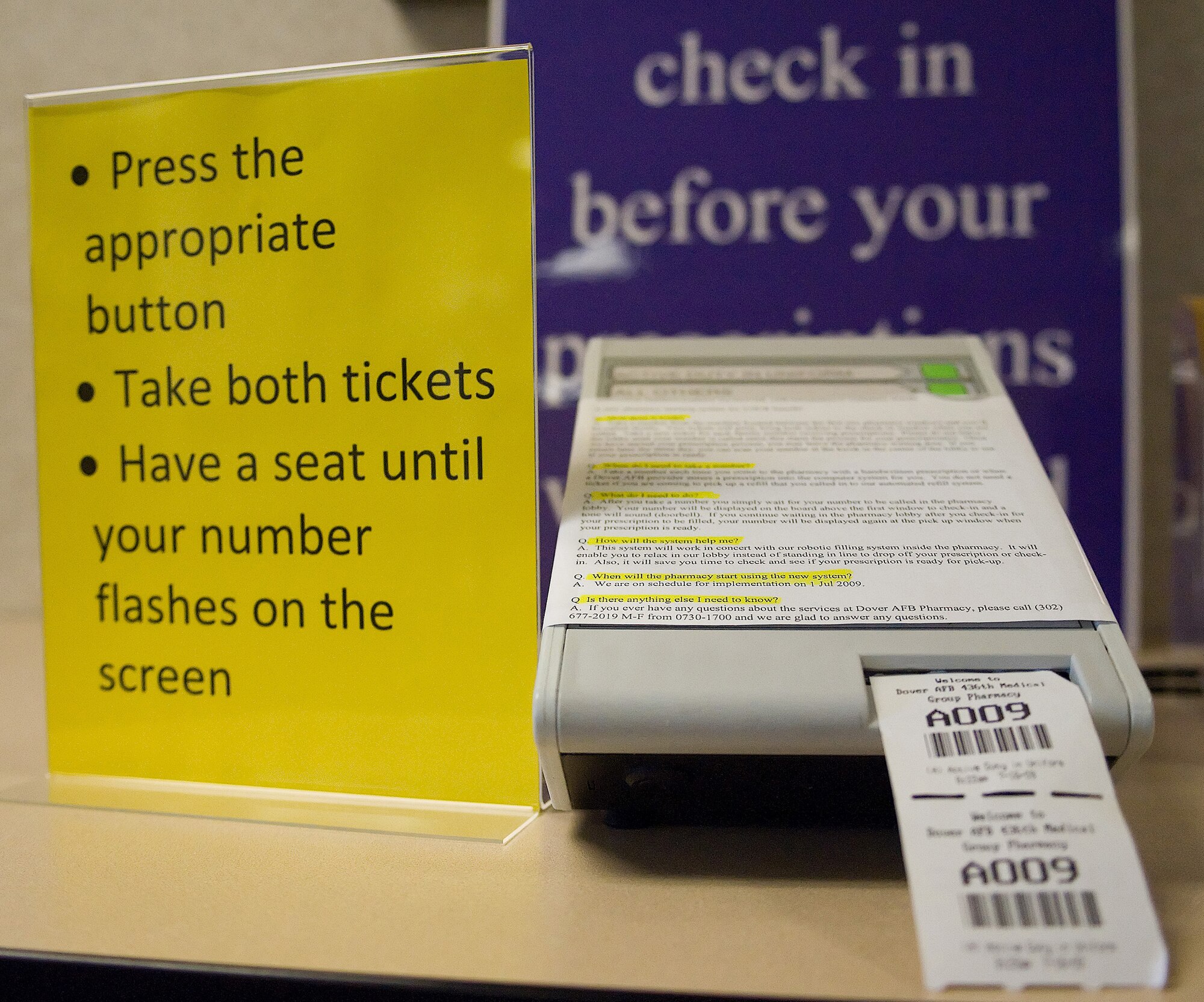 Patients needing their prescriptions filled can now use the number ticket dispenser, located in the pharmacy lobby. Patients press a button labeled ?active duty in uniform? or ?others,? keep the ticket and can take a seat in the waiting area. A ticket number will flash on the neon board along with a chiming sound. The board will indicate which counter to go to for checking in or picking up filled prescriptions. (U.S. Air Force photo/Tom Randle)