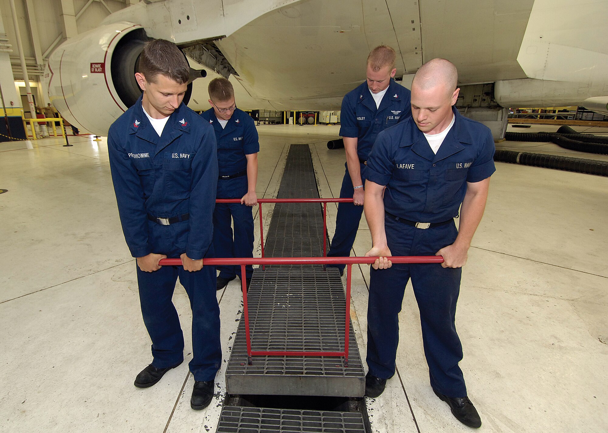 Navy maintainers use Kevin Hart’s Grating Removal Tool to lift a grate in a maintenance hangar here. The tool was created to help alleviate the stress of removing the 200-pound grates to clean the trenches. (Air Force photo by Margo Wright)