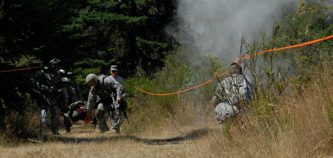 MCCHORD AIR FORCE BASE, Wash. -- Amidst the chaos of an “explosion” and smoke, 15th Security Forces Squadron members from Hickam Air Force Base, Hawaii, don gas masks and ensure their “casualty” is also protected from chemical warfare during an Air Mobility Rodeo 2009 event here July 21. The dummy weighed about 225 pounds with all its gear on. SFS specialists had to complete a course which required them to find and care for a “wounded” person, carry the litter while traversing a wooded path, take the casualty to safety, sprint to M-4 and M-9 shooting ranges, and successfully break ceramic plate targets while wearing gas masks. Hickam AFB’s team prepared for the event by doing six weeks of intense physical training including wind sprints and unconventional weight training. (U.S. Air Force photo/Staff Sgt. Carolyn Viss)