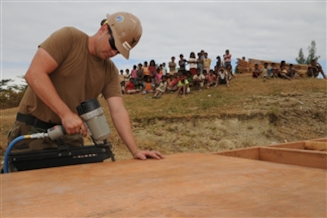 U.S. Navy Petty Officer 1st Class Edward Hourican fastens a sheet of plywood as villagers look on during a school construction project south of Baucau, Timor-Leste, on July 18, 2009.  Hourican is assigned to Naval Mobile Construction Battalion 40, a 600-person Seabee battalion that provides contingency construction, disaster relief and humanitarian assistance to the U.S. Marine Corps and other services.  