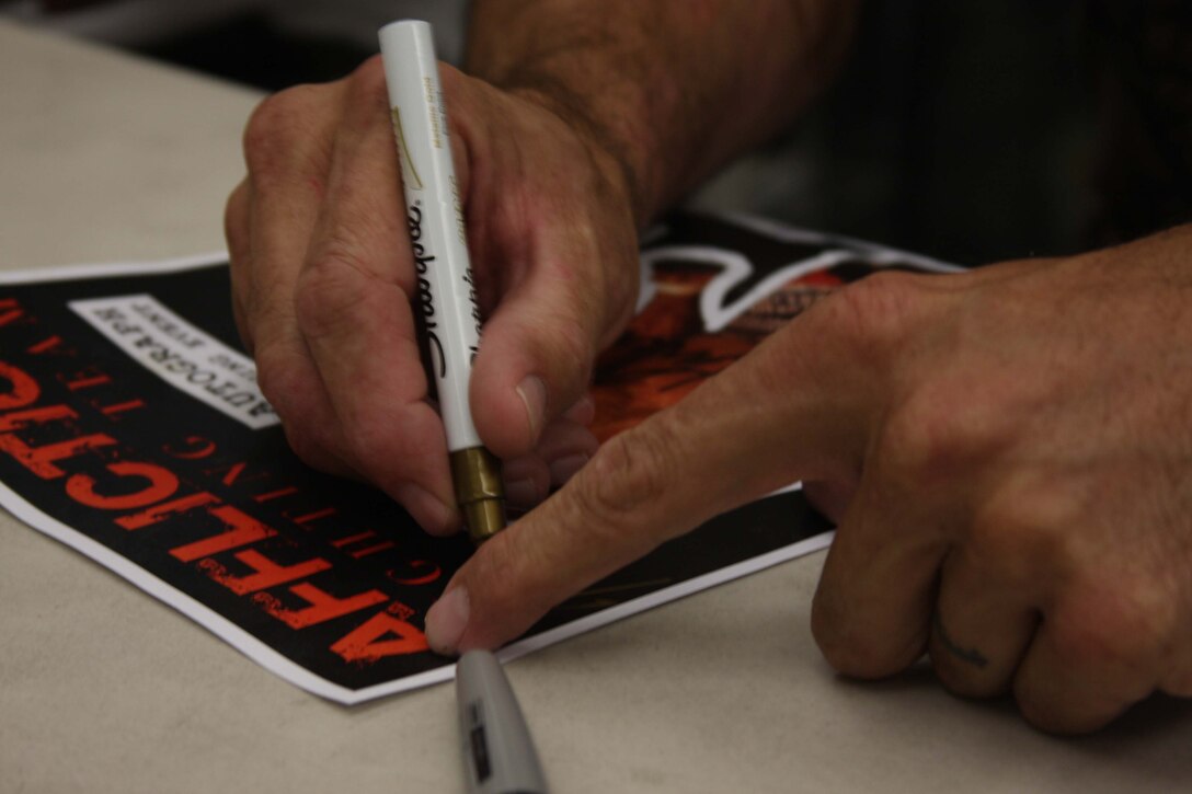 Bas Rutten, a former Ultimate Fighting Challenge heavyweight champion and member of the Affliction broadcast team, signs an Affliction poster for a Marine during an autograph and photo session at the Camp Wilson Exchange July 26.