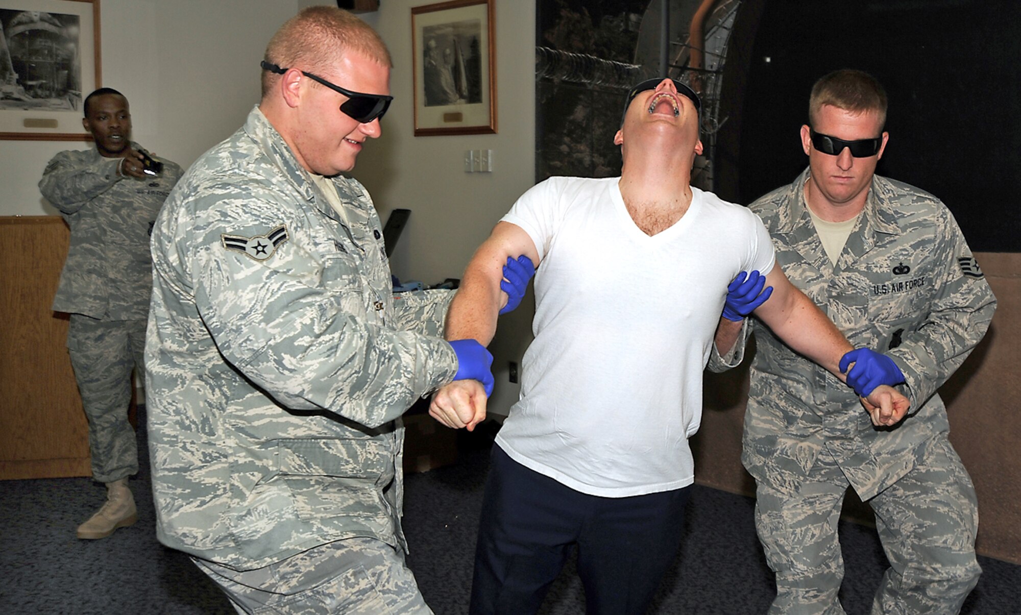 Tech. Sgt. Jerrme Stanton (far left), 721st Security Forces Squadron noncommissioned officer in-charge of training, uses an X26E Taser to subdue Chaplain (Capt.) Ronald Feeser, 21st Space Wing chapel, in a training scenario while Airman 1st Class Ryan Higgins, 721st SFS, and Staff Sergeant Daniel Chase, 721st SFS support him for safety July 20. Chaplain Feeser volunteered to assist the 721st SFS by playing the role of a suspect. This local training complies with a new Air Force Security Force training directive to certify its Airmen in the proper application of Tasers. (Air Force photo by Roberta McDonald)