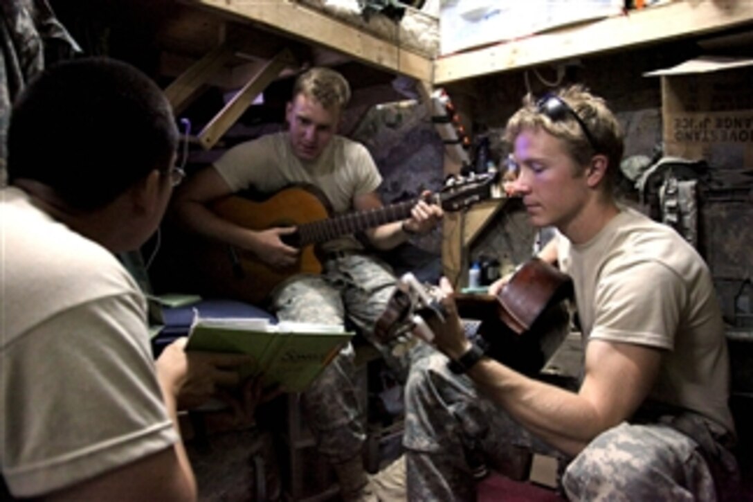 U.S. Army Spc. Paul Yi holds a book of song lyrics for Pfc. Justin Boone (2nd from right) and Sgt. Neil Hawley while they play their acoustic guitars in their living area at Combat Outpost Gorbuz, Afghanistan, on July 21, 2009.  The soldiers are deployed with Alpha Company, 425th Brigade Special Troops Battalion, 4th Brigade Combat Team, 25th Infantry Division.  