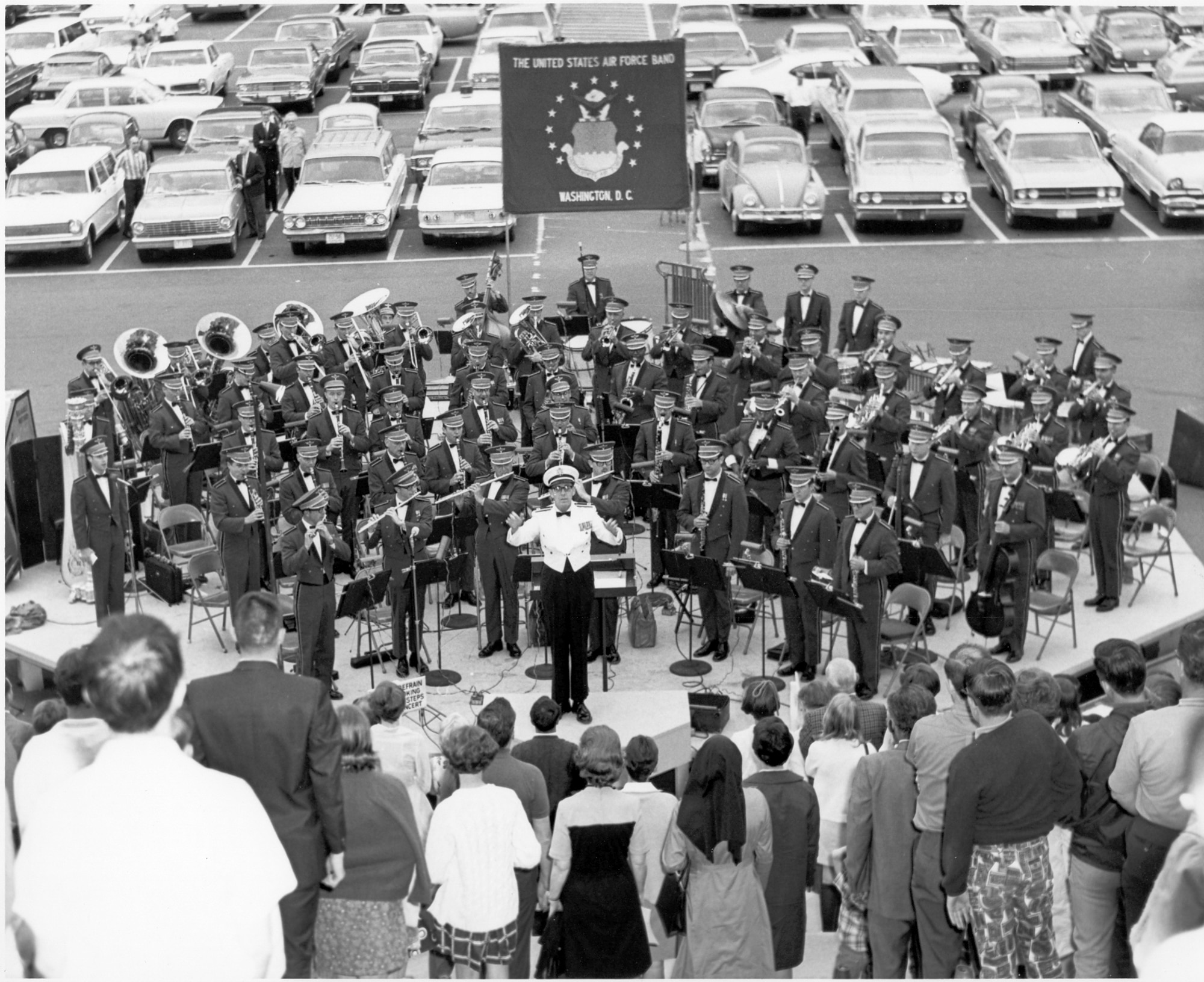 The United States Air Force Band and audience are standing as the Band begins an outdoor summer concert with the playing of the National Anthem. It is 1968 or 1969 and the concert took place on the East side of the Capitol Building.  The conductor is Captain Albert A. Bader, the assistant conductor to Lieutenant Colonel Arnald D. Gabriel, The Air Force Band's commander and conductor.  (Official photo of The Air Force Band.)