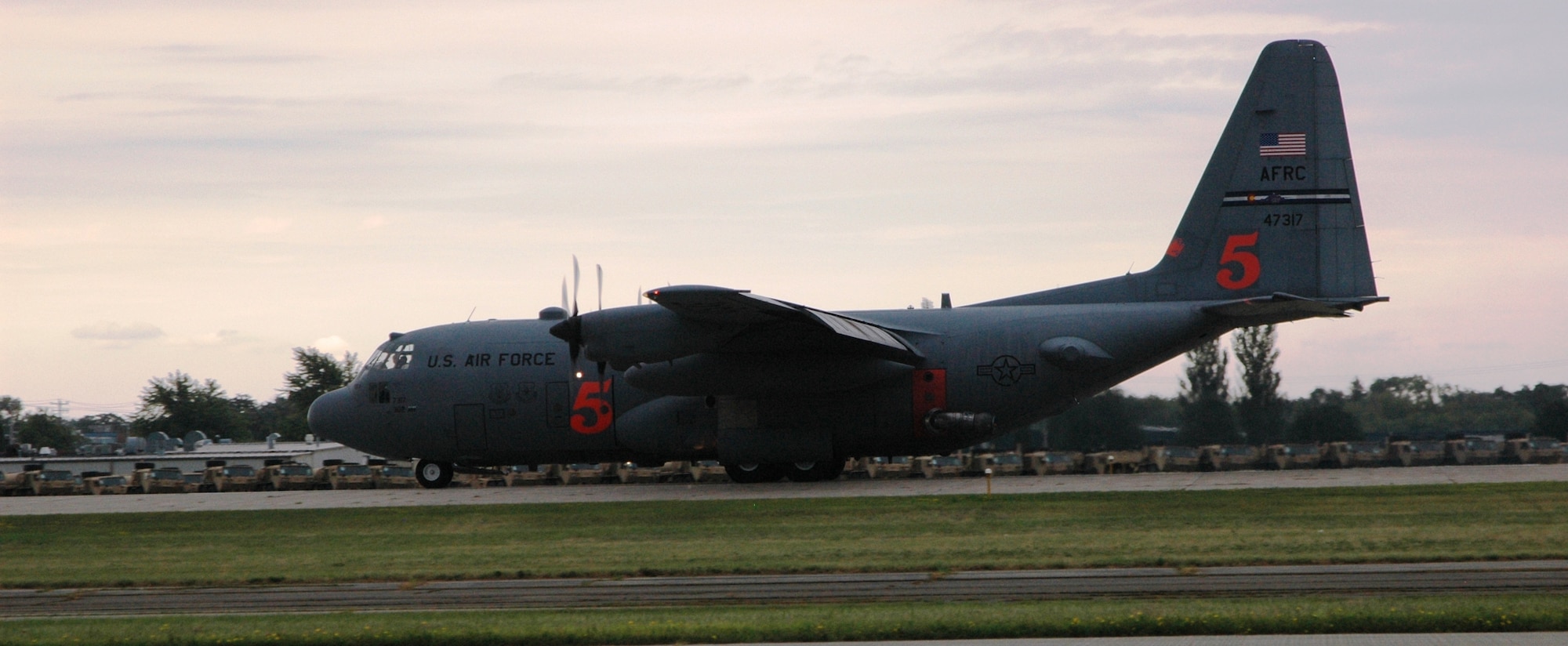 An Air Force Reserve C-130 'Hercules' equipped with the Modular Airborne Firefighting System, or 'MAFFS II,' lands after a live water drop July 27 at the Experimental Aircraft Association AirVenture airshow in Oshkosh, Wis. The airshow is known as the world's greatest aviation celebration and attracts hundreds of thousands of aviation enthusiasts from all over the world. The C-130, assigned to the 302nd Airlift Wing at Peterson Air Force Base, Colo., is equipped with the MAFFS II system and is on display at EAA AirVenture through July 29. In the background, miltiary vehicles destined for the Middle East lay in wait for transport grom the local Oshkosh truck plant line on the far side of the runway. (U.S. Air Force photo/Capt. Jeff Schoen)