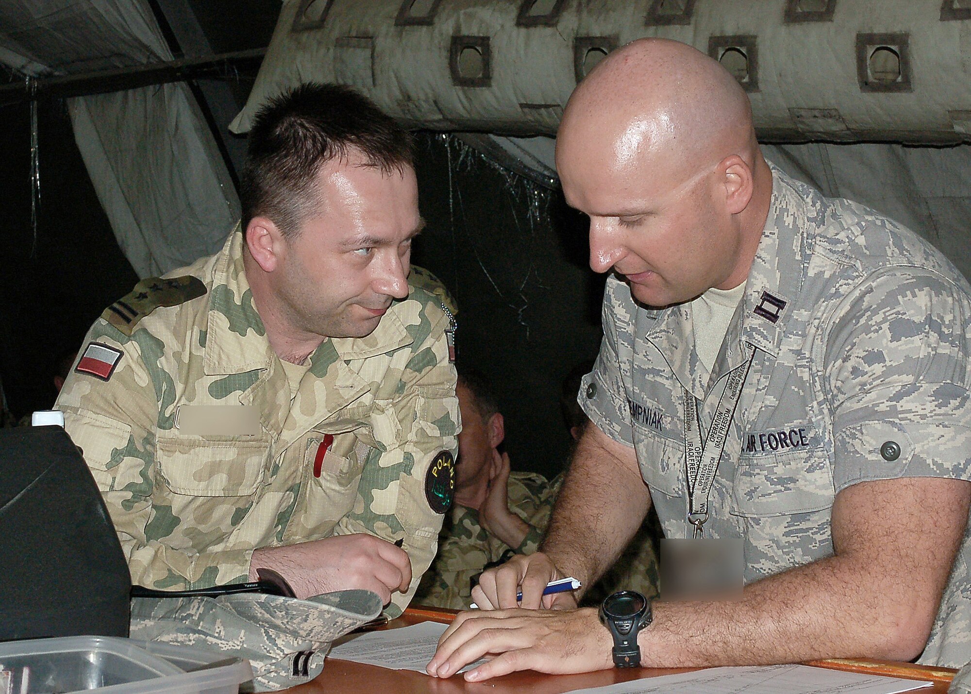 Capt. Jacek Dempniak reads and translates a document for a Polish army major transiting through the Transit Center May 20 at Manas Air Base, Kyrgyzstan. Captain Dempniak speaks six different languages and is deployed from Travis Air Force Base, Calif. Captain Dempniak is a coalition coordinator and linguist assigned to the 376th Air Expeditionary Wing. (U.S. Air Force photo illustration)