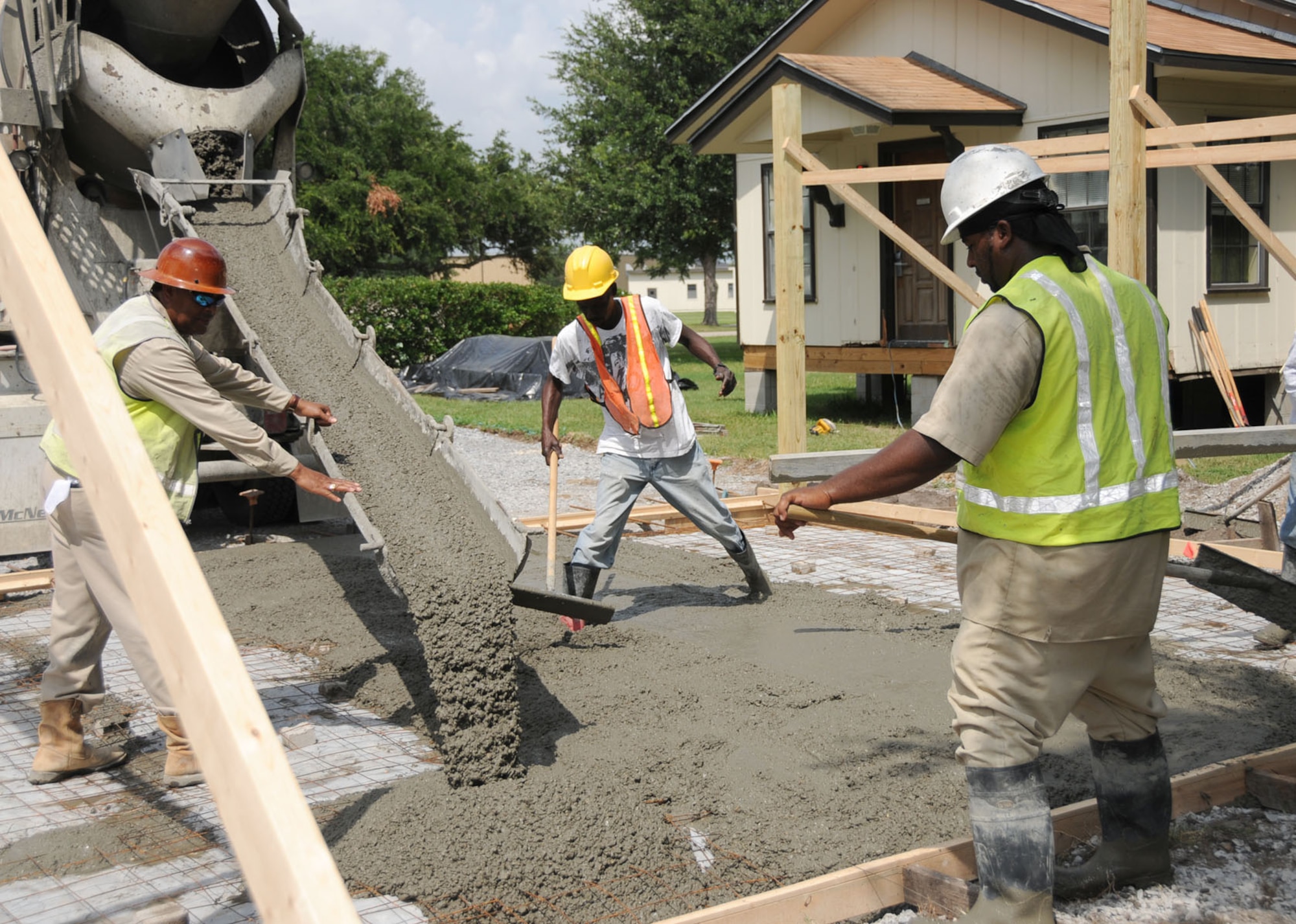 From left, Freddie Slater, Reginald Jefferson and Phillip Towner pour concrete for a new carport for Arnold Cottage, July 23.  The cottage, originally built in 1941 as quarters for distinguished visitors, bears the name of Gen. Harley “Hap” Arnold, recognized as father of the Air Force.  The frame structure was moved to the north side of Chappie James Avenue a year ago to make room for construction of a new trainer development  facility.  In addition to installing the new carport and driveway, contractors are repairing interior cracks that developed during the cottage’s move.  Interior updates are planned to make the building acceptable for future use.  (U.S. Air Force photo by Kemberly Groue)