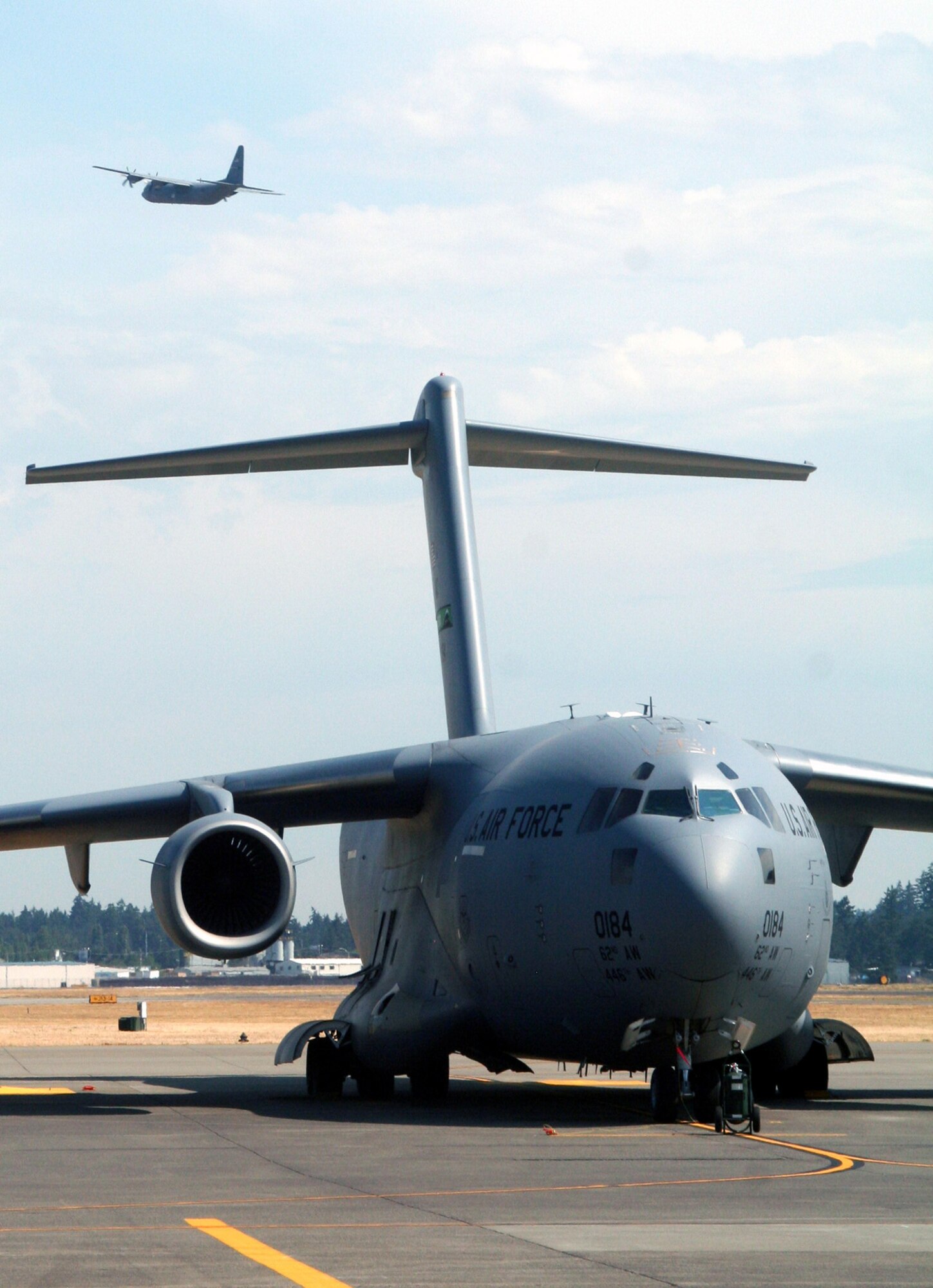 A C-17 Globemaster III from the 62nd Airlift Wing is parked on the flightline at McChord Air Force Base, Wash., July 25, 2009, while a C-130J Hercules from the 19th Airlift Wing, Little Rock AFB, Ark., takes off.  The C-17 and the C-130J are some of Air Mobility Command's main airlift aircraft that helps provide "global reach" and the Air Force to "fly, fight and win...in air, space and cyberspace." (U.S. Air Force Photo/Tech. Sgt. Scott T. Sturkol)