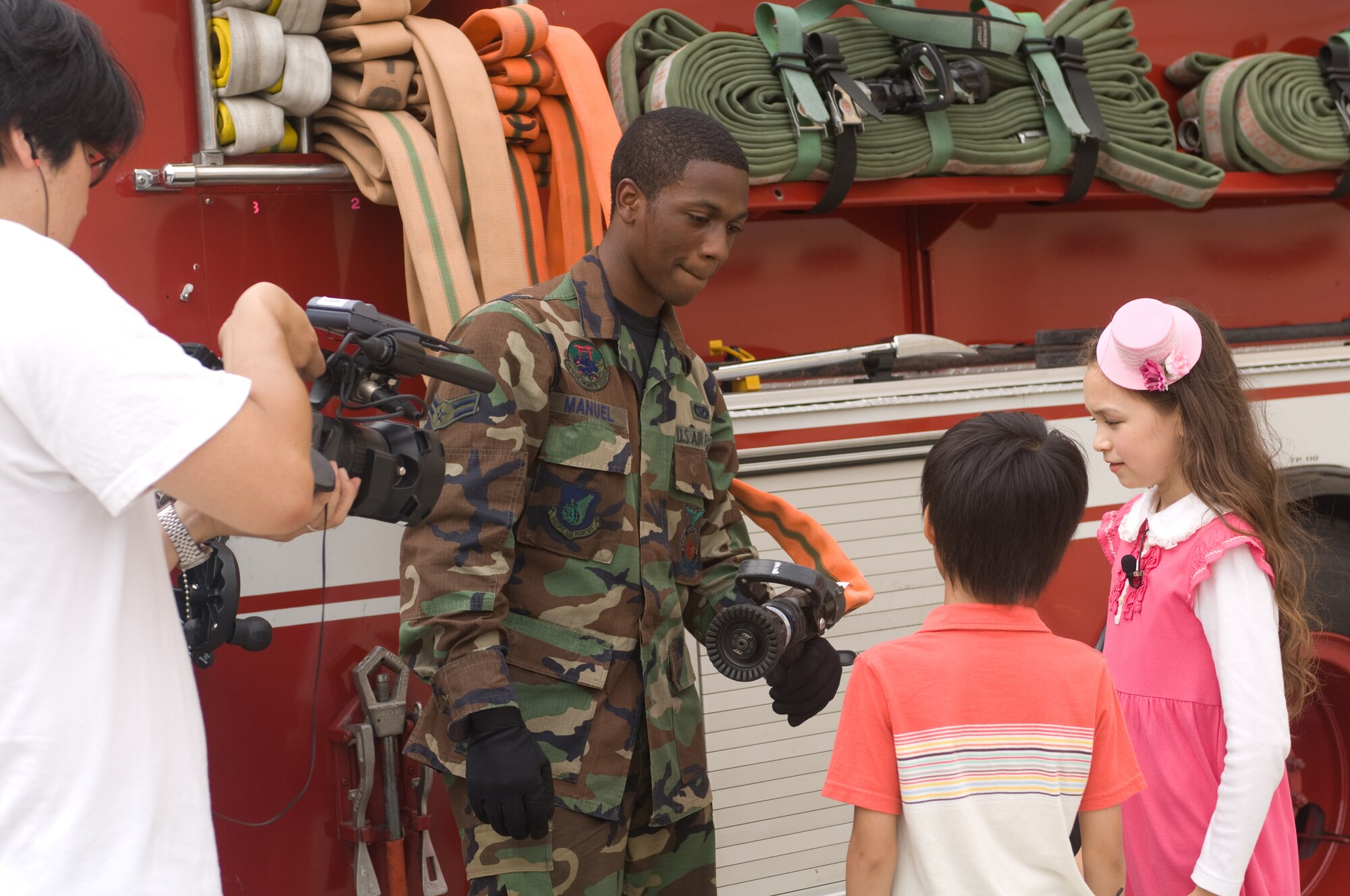 YOKOTA AIR BASE, Japan -- Airman 1st Class Taylor Manuel, 374th Civil Engineer Squadron firefighter, talks with the stars of TV Tokyo's children's television show "OHA, STA" during a visit to the base fire department July 29. Ariel Jasmin Bukowsky (right) helps Shion Kikuchi speak with various native English speakers during the show. Base firefighters gave the children an in-depth tour of fire trucks and even let the children try on fire-fighting gear. (U.S. Air Force photo/Osakabe Yasuo)