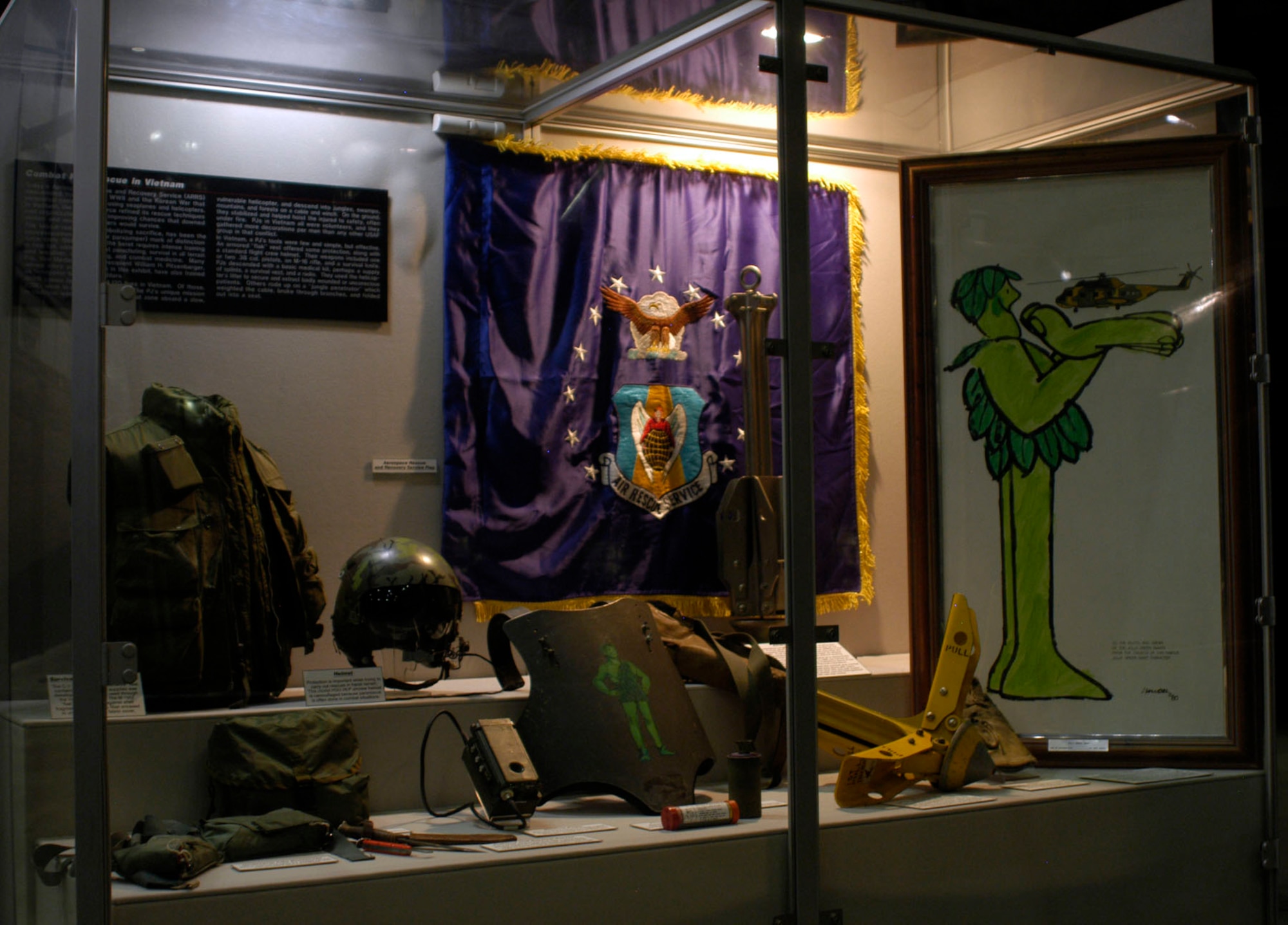 DAYTON, Ohio - The Combat Pararescue in Vietnam exhibit in the Southeast Asia War Gallery at the National Museum of the U.S. Air Force. In this exhibit, (counter clockwise from the flag) an Aerospace Rescue and Recovery Service flag, an HGU-26/P aircrew helmet, a C-1 "emergency sustenance" vest and M-1952 "flak" vest, an LPU-10/P underarm life preserver, a medical kit, fighting and survival knives, a survival radio, helicopter crew body armor, smoke grenade and combination smoke illumination flare, jungle penetrator, glove, "Jolly Green Giant" painting by Saul Mandel and another jungle penetrator. (U.S. Air Force photo)