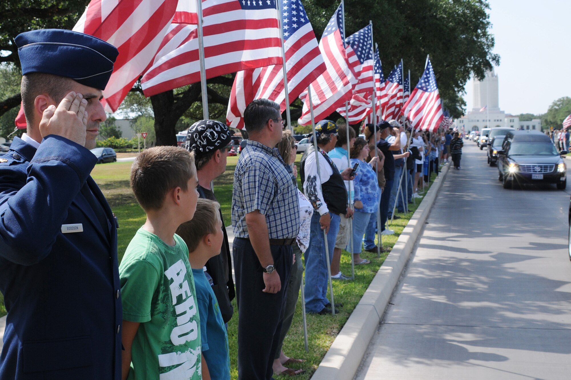 Maj. J.T. Goodson salutes the motorcade carrying the casket of Marine Corps Lance Cpl. Brandon Lara as his sons, Hunter (second from left) and Logan, watch the vehicles make their way down Harmon Drive July 26 at Randolph Air Force Base, Texas. (U.S. Air Force photo/Don Lindsey) 
