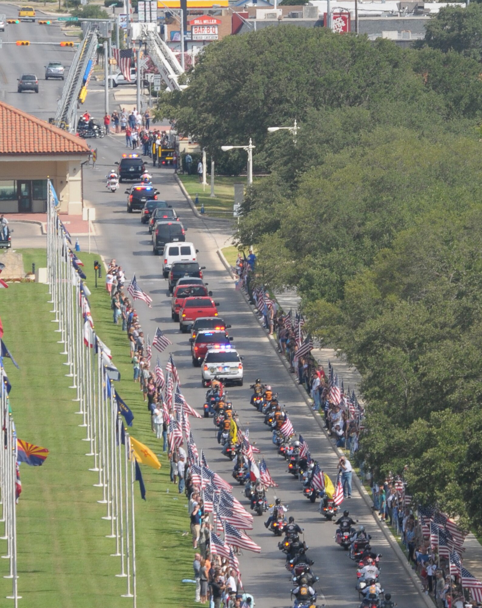 The motorcade carrying the casket of Marine Corps Lance Cpl. Brandon Lara passes under a flag suspended between the extended ladders of fire trucks from Live Oak, Texas, and Universal City, Texas, July 26 as it exited Randolph Air Force Base, Texas. The motorcade is trailed by more than 100 motorcyclists of the Patriot Guard Riders. (U.S. Air Force photo/Joel Martinez) 
