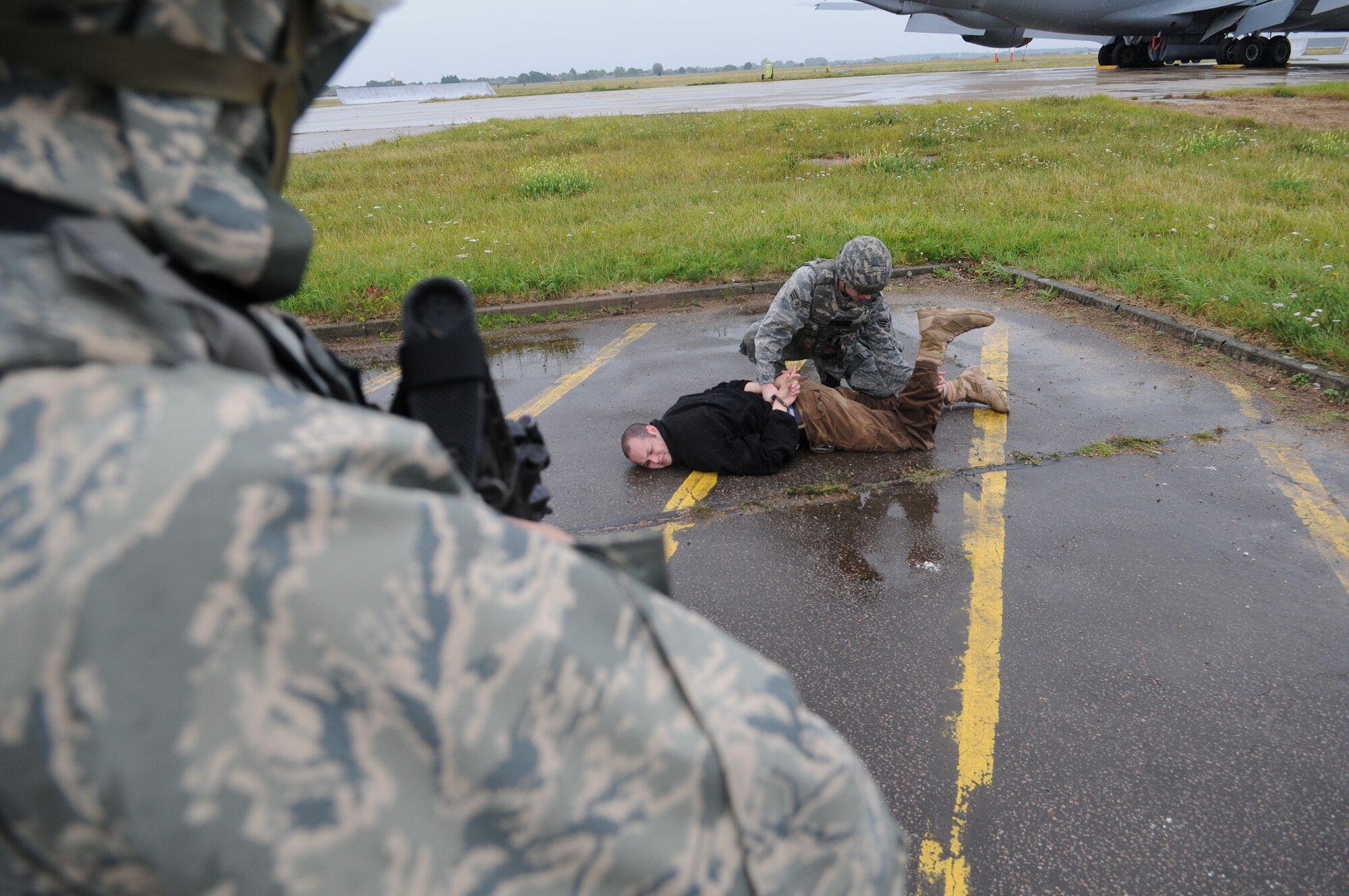 RAF MILDENHALL, England -- A 100th Security Forces Squadron Airman provides overwatch while his wingman searches a detainee who attempted to sneak into Base X in the trunck of a car July 21. A Phase II exercise was conducted here July 20-22 south of the flightline in preparation for an upcoming Operational Readiness Inspection. (U.S. Air Force photo by Senior Airman Thomas Trower)
