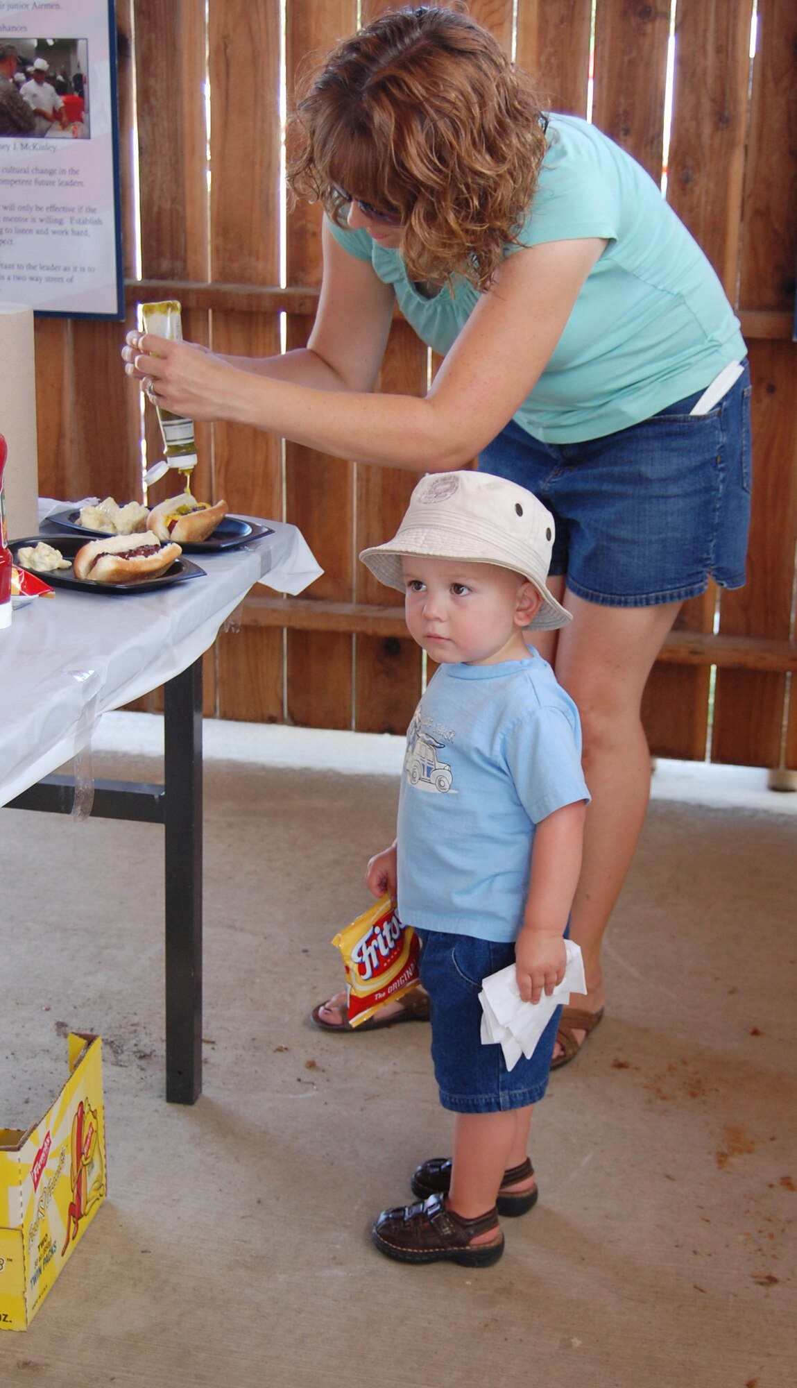 Little Warrior Nathan, 2, watches the crowd forming in the food tent while waiting for his mom, Sara, to finish getting their hot dogs ready. Team Malmstrom members and their families were treated to a free picnic July 24 at Sun Plaza Park, sponsored by the Military Affairs Committee, 1st Liberty Federal Credit Union, the 341st Force Support Squadron and several other local businesses. (U.S. Air Force photo/Valerie Mullett)