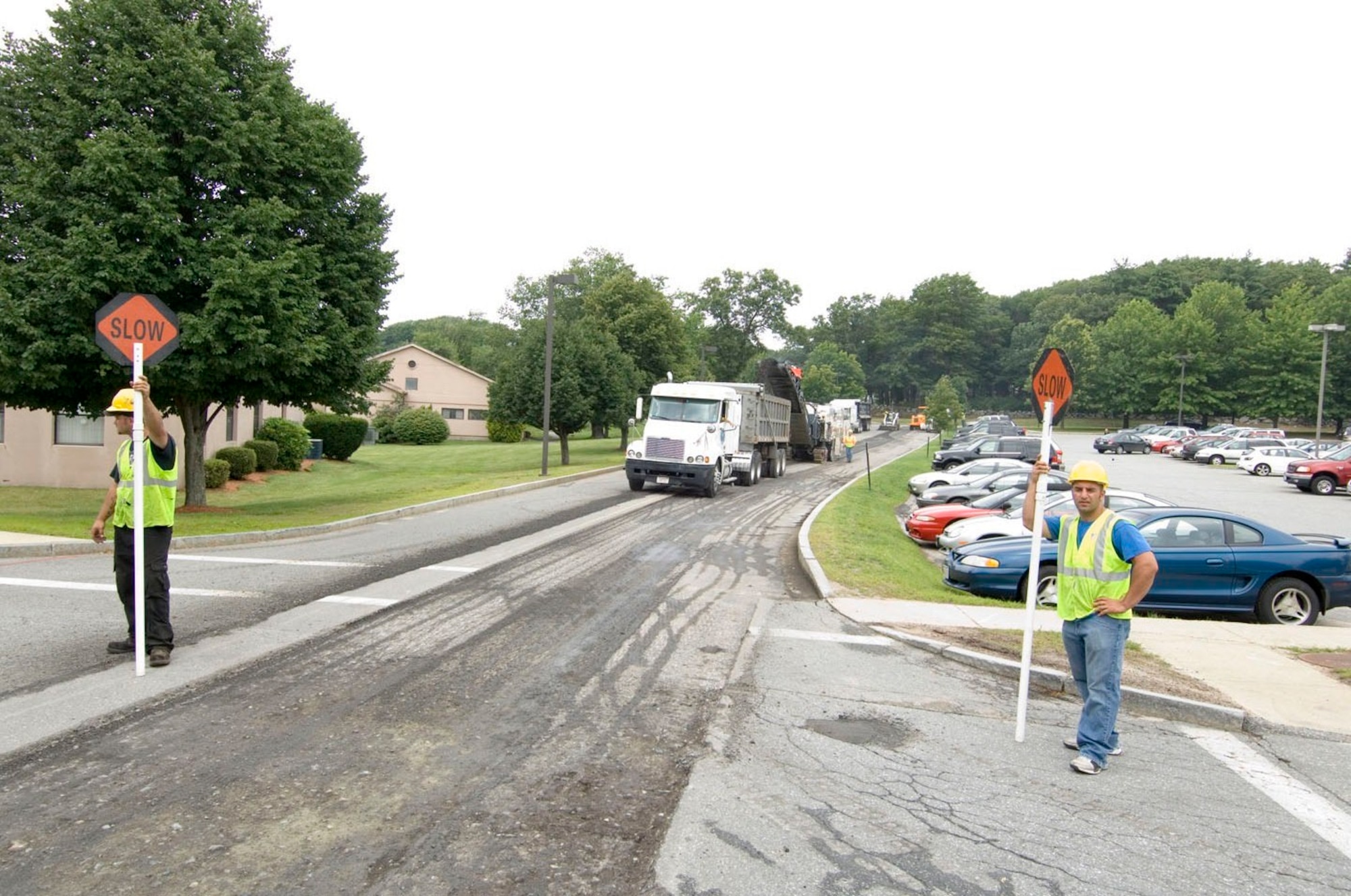 Contractors from Hanscom Civil Engineering direct traffic during a road re-paving project on July 16 as their asphalt milling machine removes the last strip of old asphalt on Bestic Drive between Barksdale Street and Schilling Circle.  (U.S. Air Force photo by Rick Berry)