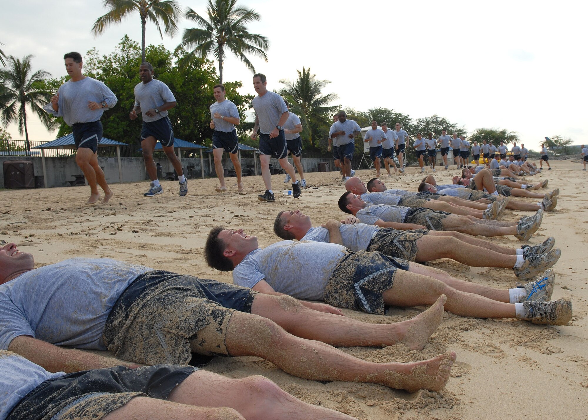Senior Master Sgt. JJ Little, Pacific Air Forces’ Inspector General team, leads a group of Air Force personnel past another group performing calisthenics  in the sand at Hickam Air Force Base, Hawaii, May 27. Approximately 70 people participated in the physical training session, which included a 1.5-mile run to Hickam Beach, a half-hour session of calisthenics and team building, followed by a 1.5-mile run back to the starting point. The directorates participating in the beach session were A3, A4, A5 and A8. (U.S. Air Force photo/Tech. Sgt. Jerome Tayborn)