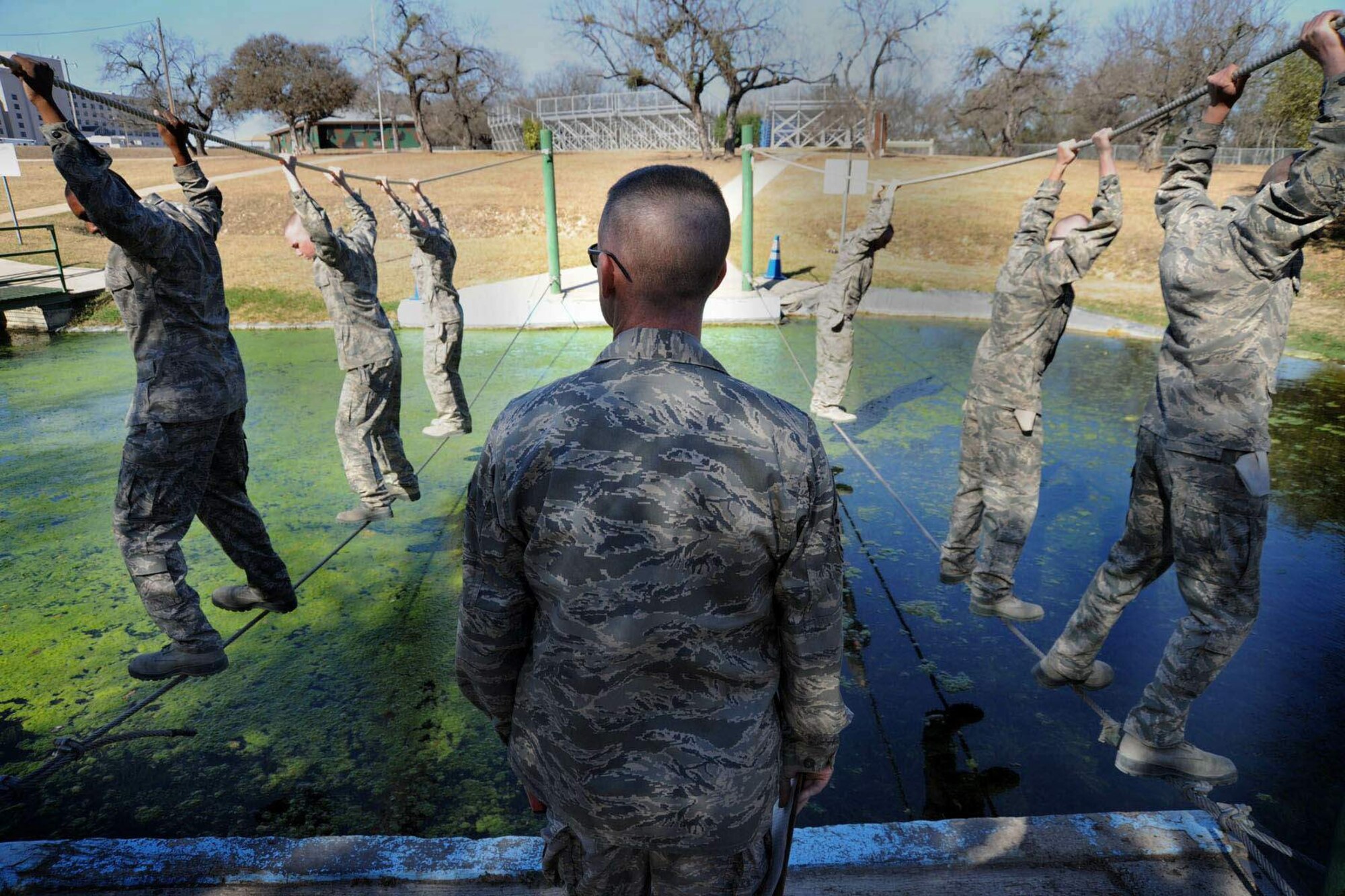 At the obstacle course at Lackland Air Force Base, Texas, basic trainees are watched by a military training instructor as they pass over an algae-filled water obstacle on a cable and rope bridge. These trainees are on their way to becoming ?warrior Airmen.? (U.S. Air Force photo/Michael Tolzmann)