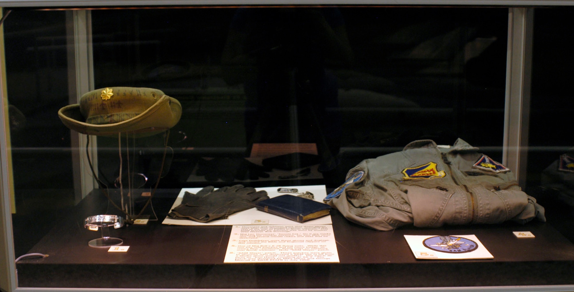 DAYTON, Ohio - Items on display in the First In, Last Out: Wild Weasels vs. SAMs exhibit: 1) Thorsness and Johnson were shot down eleven days after their decorated mission, spending the rest of the war as POWs in North Vietnam. This POW bracelet for Johnson was worn by another Wild Weasel, Bob Dorrough. 2) Maj. Leo Thorsness' "boonie hat." On it are marks showing his combat missions, his two MiG victories and several missile radars and sites that he destroyed. 3) Capt. Dethlefsen wore these gloves and dogtags and carried the Bible and fingernail clippers on this mission. 4) One of Maj. Bell's K-2B flying suits. While this one has unit patches and his name badge, aircrews flew "sanitized" flying suits on missions over North Vietnam. Note "SAM Slayer" patch. 5) "SAM Slayer" patch donated by Col. Mike Gilroy, USAF (ret.). These patches were given to aircrews who destroyed a SAM site (a hit from a Shrike alone would not qualify). The patch depicts an "Iron Hand" crushing an SA-2. The patch was designed by Mike Gilroy and George Metcalf at Takhli RTAFB in July 1966. (U.S. Air Force photo)