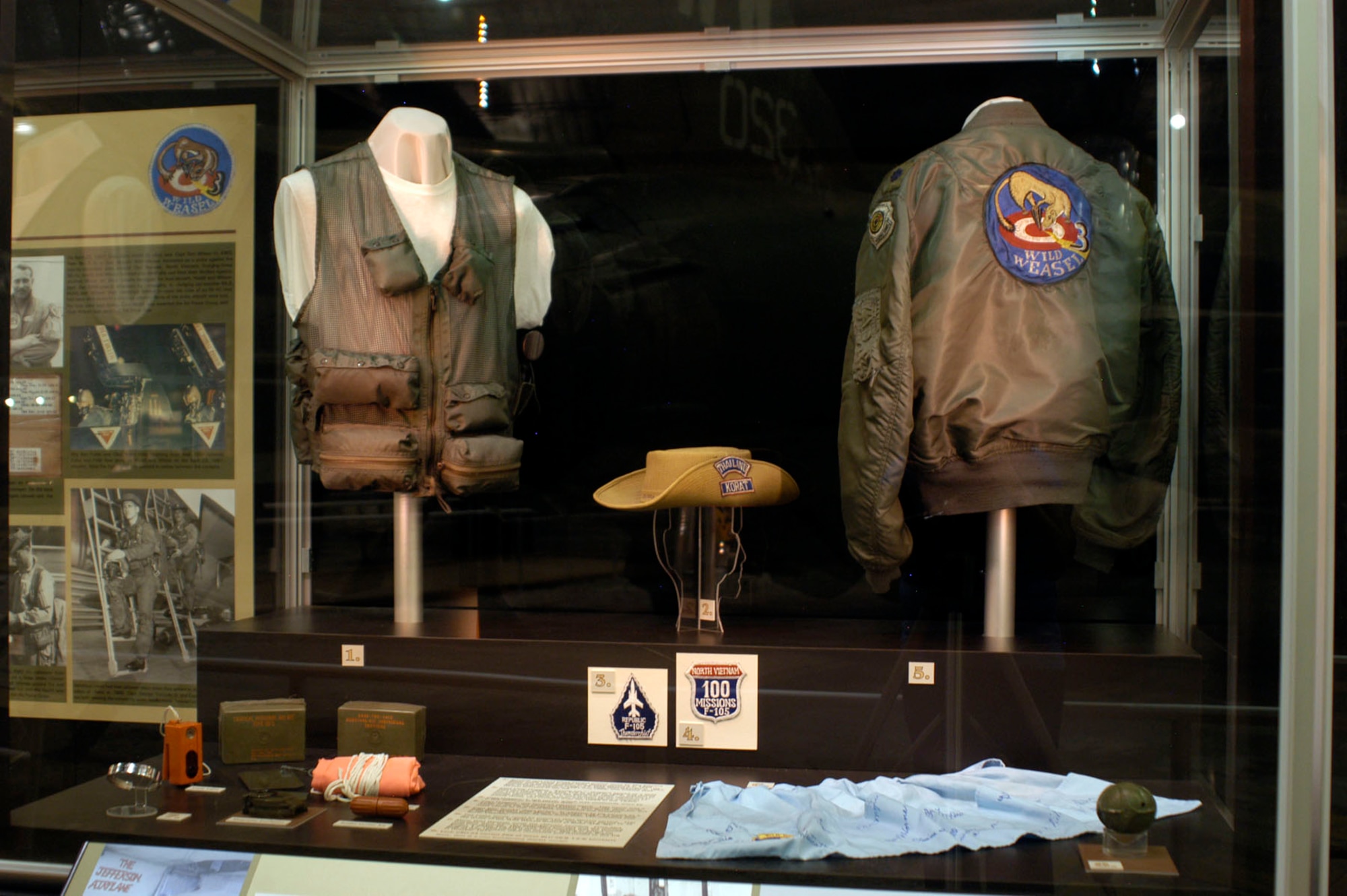 DAYTON, Ohio - In the First in, Last Out: Wild Weasels vs. SAMS exhibit: 1) Survival vest worn by Maj. Edward White while flying F-105F WIld Weasel missions in 1968. White was heavily involved in the Wild Weasel program. He deployed with the first group of F-100F Wild Weasels in 1965, flew F-105F missions in 1967 and 1968 and trained Wild Weasel aircrews in the U.S. 2) Capt. Larry Huggins' "boonie hat." Huggins served as a Wild Weasel pilot with th 44th TFS at Korat in 1968 and retired from the USAF as a brigadier general in 1989. In addition to the 113 mission marks on the hat, is his name spelled out in Cyrillic (Russian) letters. It was written by the "Russian exchanged pilot," a fellow airman and naturalized American whose family had escaped from Russia in the 1930s. 3) Capt. Huggins' F-105 patch, which was commonly worn by F-105 aircrews in Southeast Asia. 4) Capt. Huggins' 100 mission patch. This patch was a badge of honor for pilots and EWOs. Technically, they could return to the U.S. after 80 missions over North Vietnam, but most chose to stay until they completed 100. 5) Capt. Billy Sparks' flight jacket. In addition to his service as a Wild Weasel pilot from March to October 1967, he also flew F-105Ds. All together, he flew more than 140 missions over North Vietnam. 6) The entire family could be proud of Wild Weasel service. This apron belonged to Sparks' wife, Dell, and it was signed by all the wives of the Wild Weasel school at Nellis AFB. 7) Many Wild Weasels made the ultimate sacrifice. POW/MIA bracelets were worn to remember prisoners and the missing until they returned. This POW/MIA bracelet was for Donald Singer, a 354th TFS EWO who went missing in action on Aug. 17, 1966 (along with his pilot, Maj. Joseph Brand). Both of their remains were recovered and returned to the U.S. in October 1977. 8) Each CBU-24 carried 665 of these BLU-26/B 1.2-lb. bomblets. (U.S. Air Force photo)