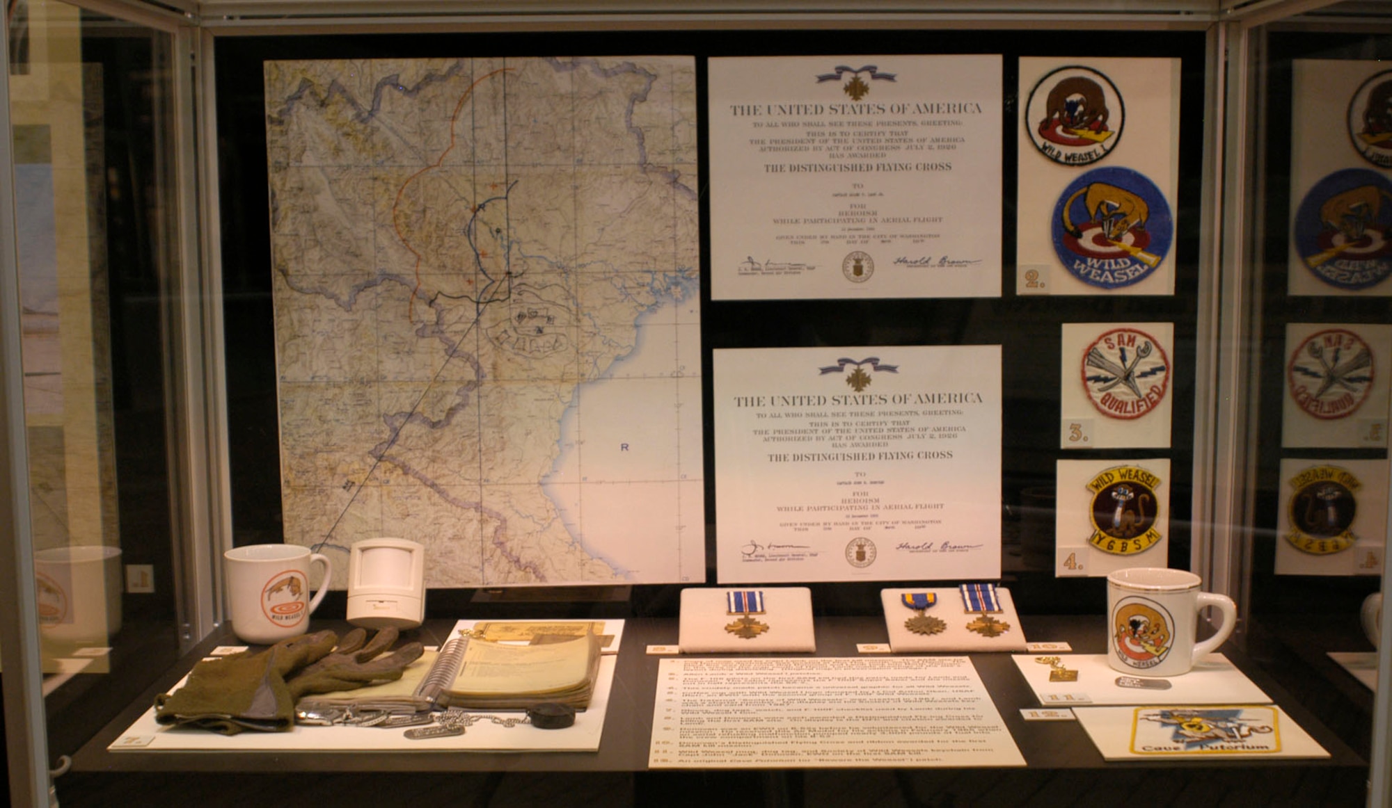DAYTON, Ohio - In this photo: Map used by Capt. Lamb on the first kill mission. The SAM site he and Donovan destroyed was located at Phy Tho, northwest of Hanoi. The black line was the route that Donovan and Lamb took into North Vietnam. In the area on the map south of Hanoi, Lamb made drawings of the site's layout during debriefing. Gloves, dog tags, watch and F-100F checklist used by Lamb during his Wild Weasel I tour. Lamb and Donovan were each awarded a Distinguished Flying Cross for killing the first SAM site. On display is the DFC and citation awarded to Lamb. The F-105 pilots on the first SAM kill had this patch made for Lamb and Donovan for killing the first SAM site. This saber represents to F-100F Super Sabre and the missile cut in half represents to SA-2. Allen Lamb's Wild Weasel I patches. This crudely made patch became a universal graphic for all Wild Weasels. An original Cave Putorium (or "Beware the Weasel") patch. The fraternal "Society of Wild Weasels" was created in 1967, and Lamb was a charter member. On display are his Society of Wild Weasels key chain and card from 1967. Coffee cup with Wild Weasel I logo donated by Lt. Col. Arthur Oken, USAF (ret.), an EWO with the second group of F-100F Wild Weasels. Donovan was an EWO on B-52s before he volunteered for the Wild Weasels mission. He received this air medal for his actions in February 1965 when an aerial refueling malfunctions pumped nearly 3,000 pounds into the fuel into the crew compartment on his B-52. Wild Weasel mug, dog tag and Society of WIld Weasels keychain from Capt. John "Jack" Donovan, EWO on the first SAM kill. (U.S. Air Force photo)