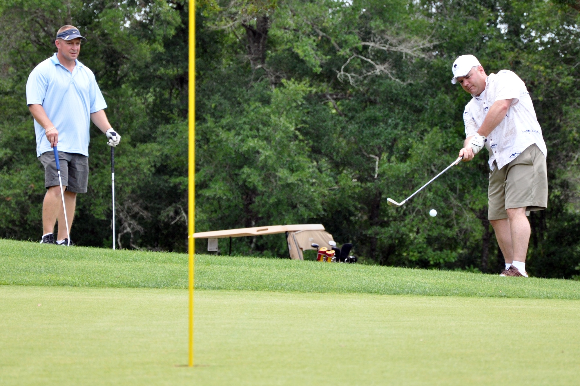 EGLIN AIR FORCE BASE, Fla. – Bernie DeLong takes a chip shot while Senior Master Sgt. Christopher King, 96th Aero Medical Dental Squadron, watches during a golf tournament at the Eglin Golf Course May 29. The tournament was a fundraiser to support the Hearts Apart Dining program, a program that offers free dining to the families of deployed servicemembers. The goal for the event, led by the First Sergeant’s Council, was to raise $4,000 with 100 percent of the proceeds going to the program. More than 115 people participated in the tournament. (U.S. Air Force photo/ Airman Anthony Jennings)
